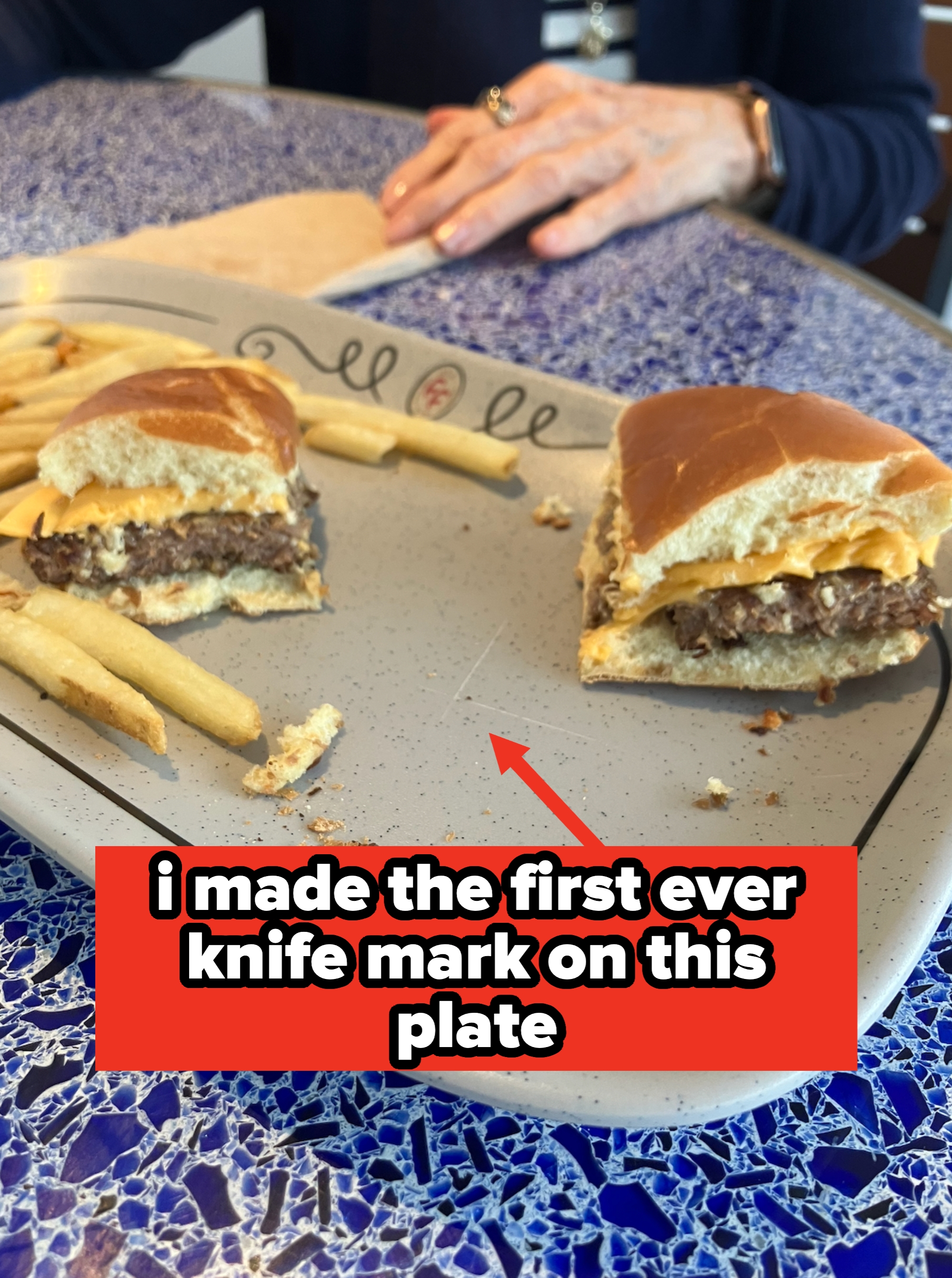 Burger and fries connected  a speckled plate, with a person’s hands resting successful  the background