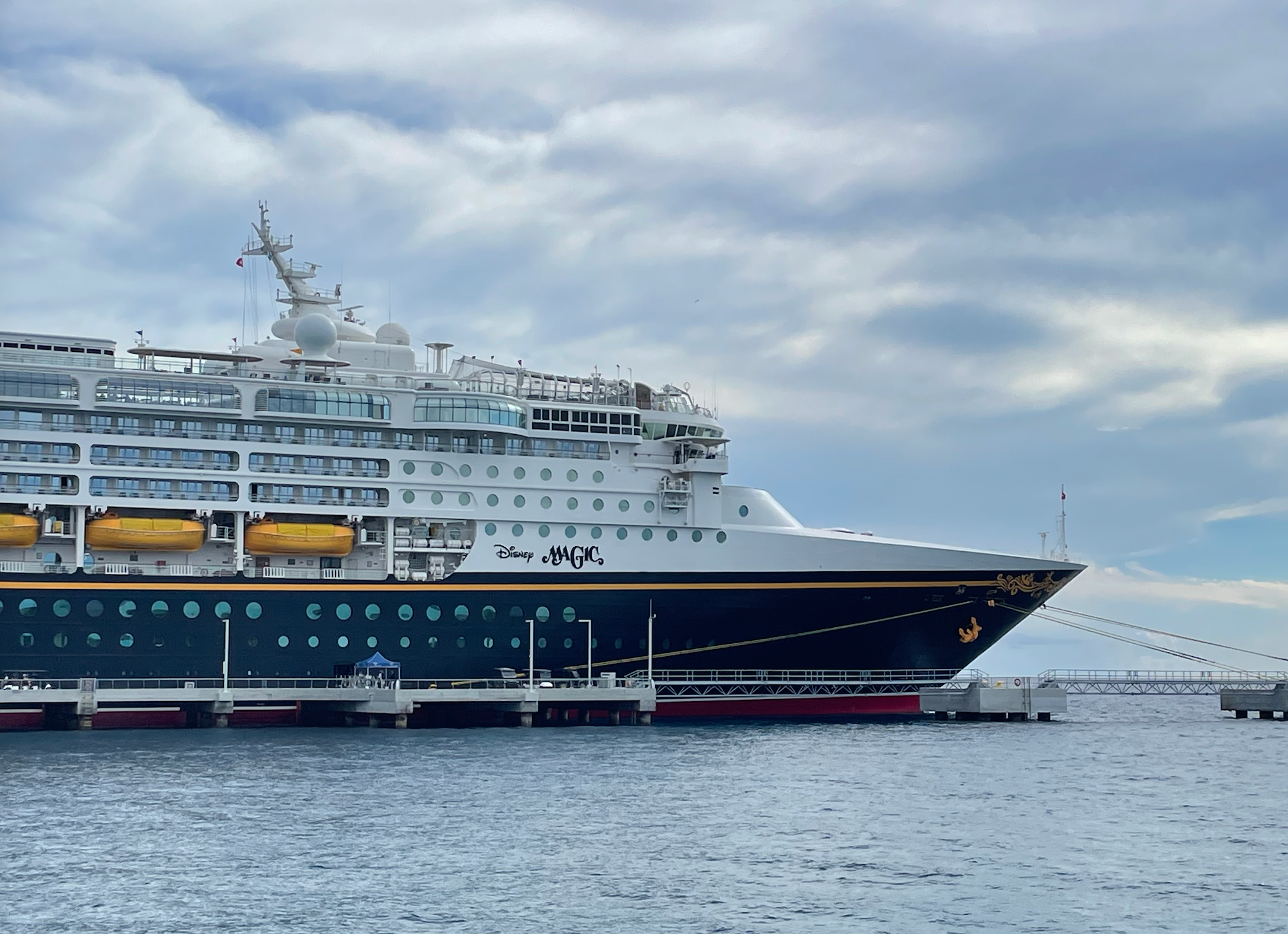 Cruise vessel  docked astatine  a pier with "Disney Magic" substance   connected  the side, acceptable   against a cloudy entity  backdrop
