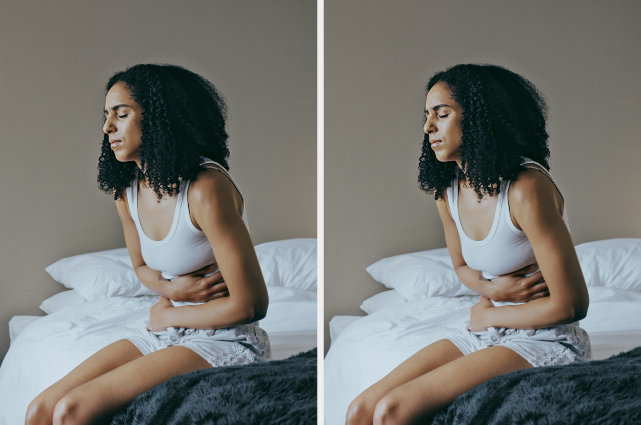 Person sitting on a bed, holding their stomach with a pained expression, possibly experiencing discomfort or cramps