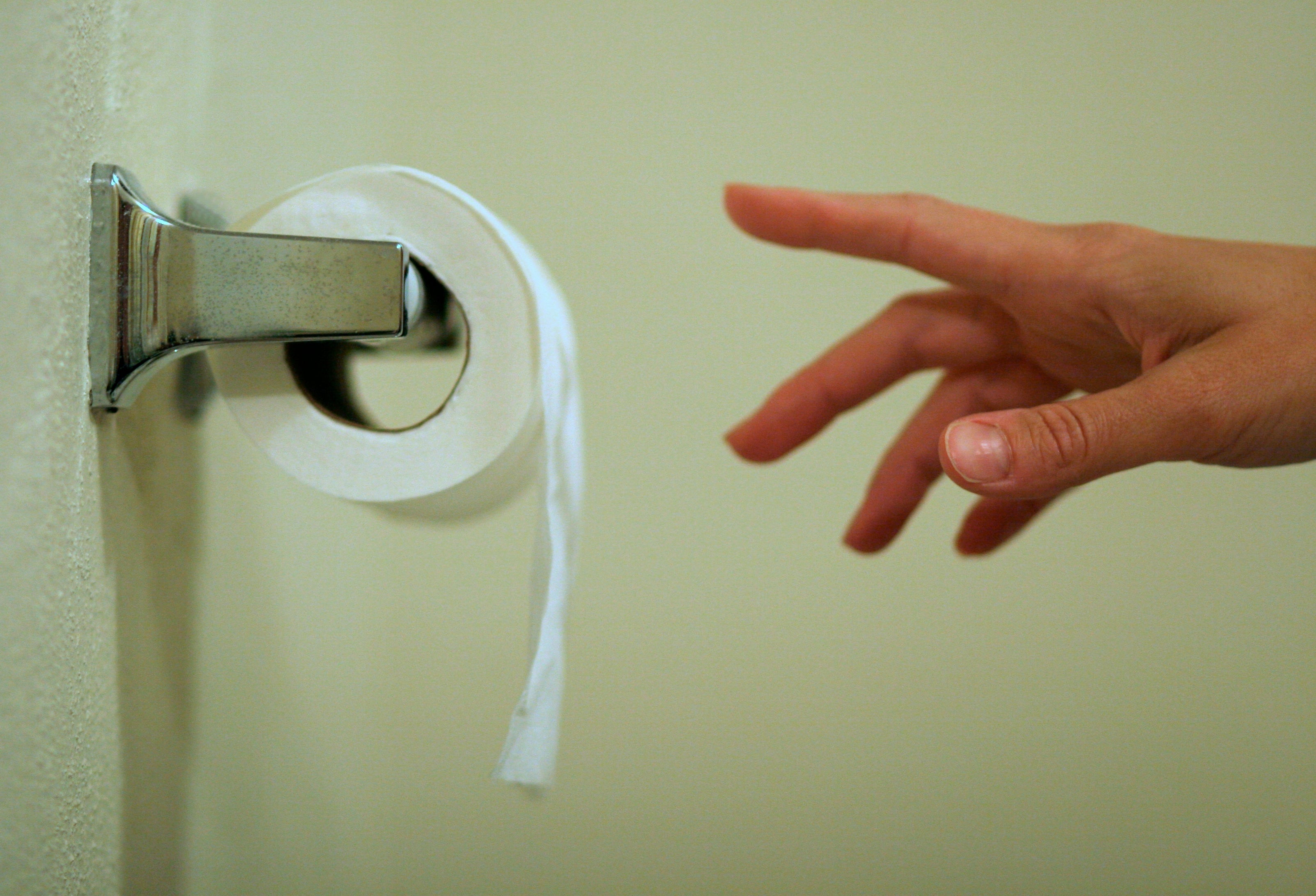 Hand reaching for a roll of toilet paper on a wall-mounted holder