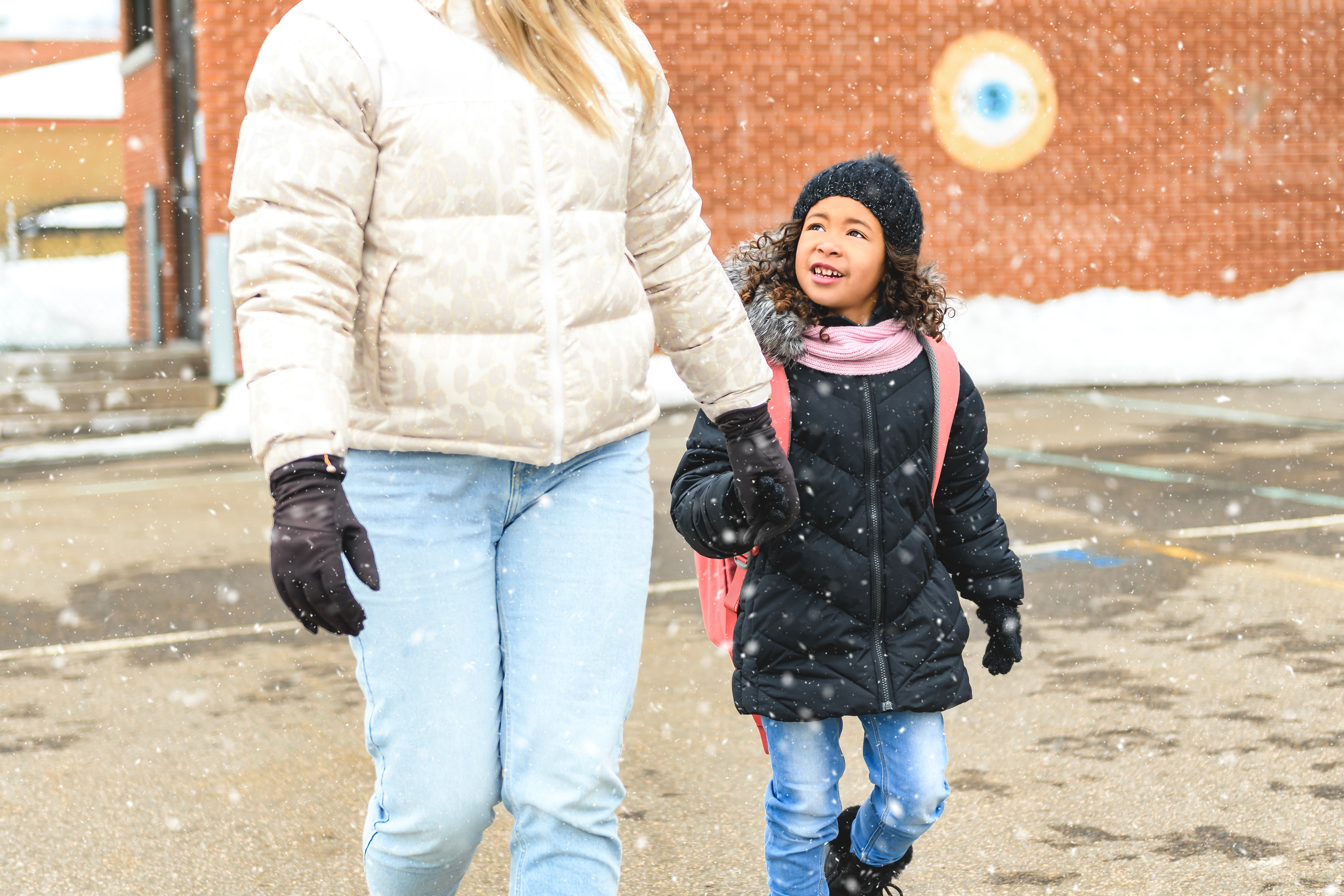 Adult and kid  successful  wintertime  covering  locomotion  hand-in-hand done  lightly falling snow, smiling and chatting