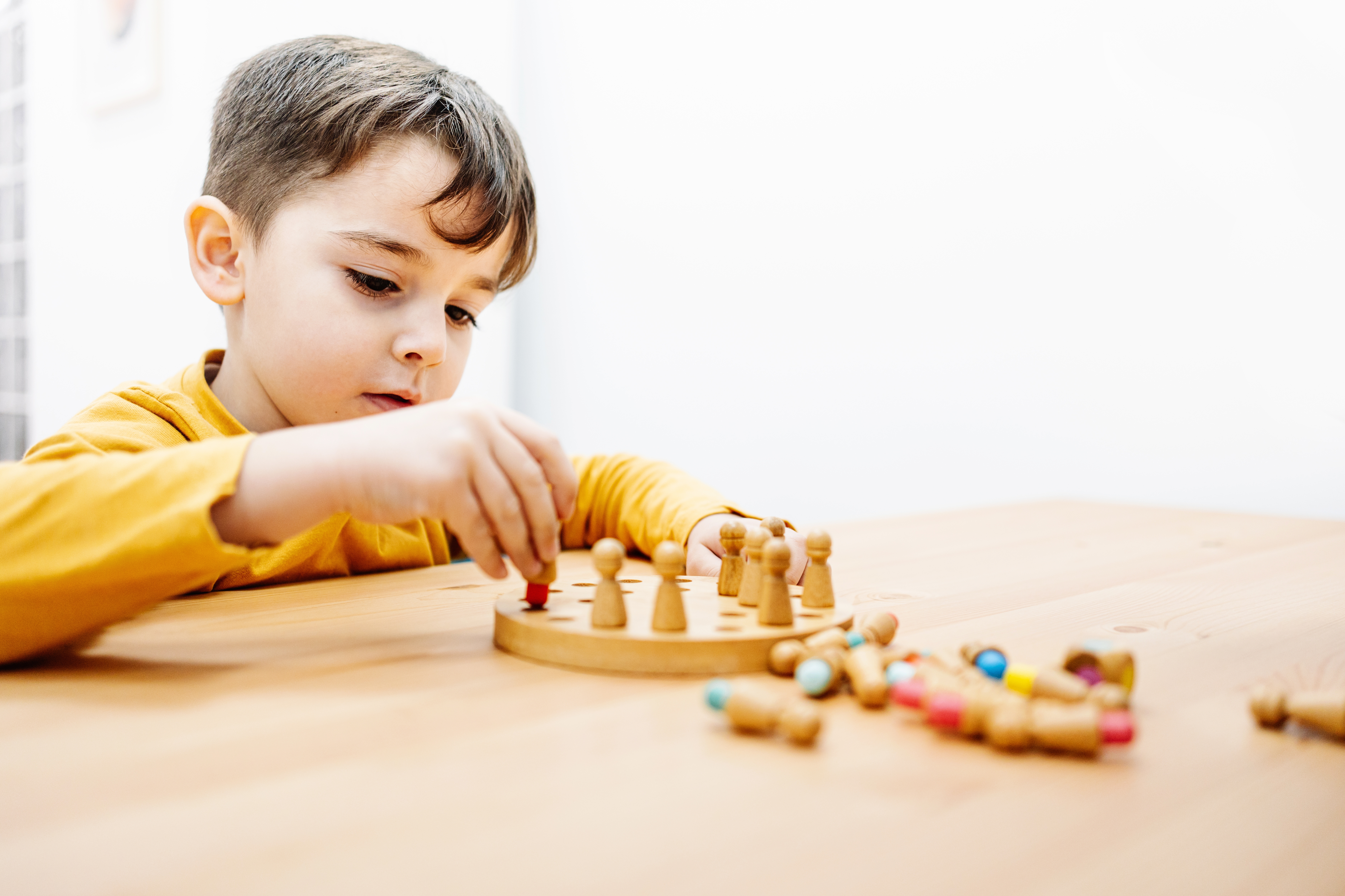 Child focusing intently portion    playing a woody  committee  crippled  with tiny  pegs and colorful tokens connected  a table