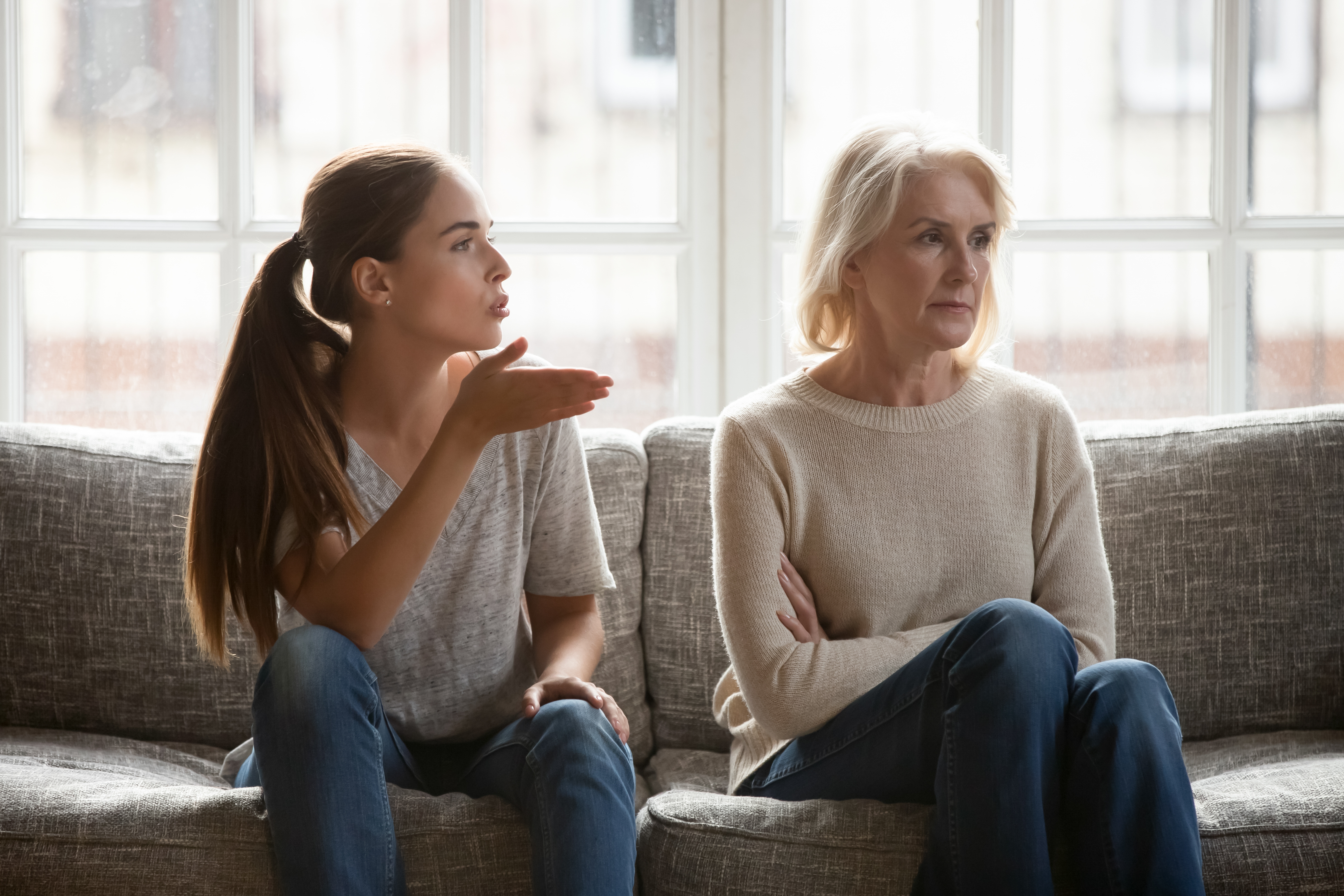 Mother and girl  sitting connected  a couch, 1  gesturing portion    talking, the different   looking distant  with folded arms