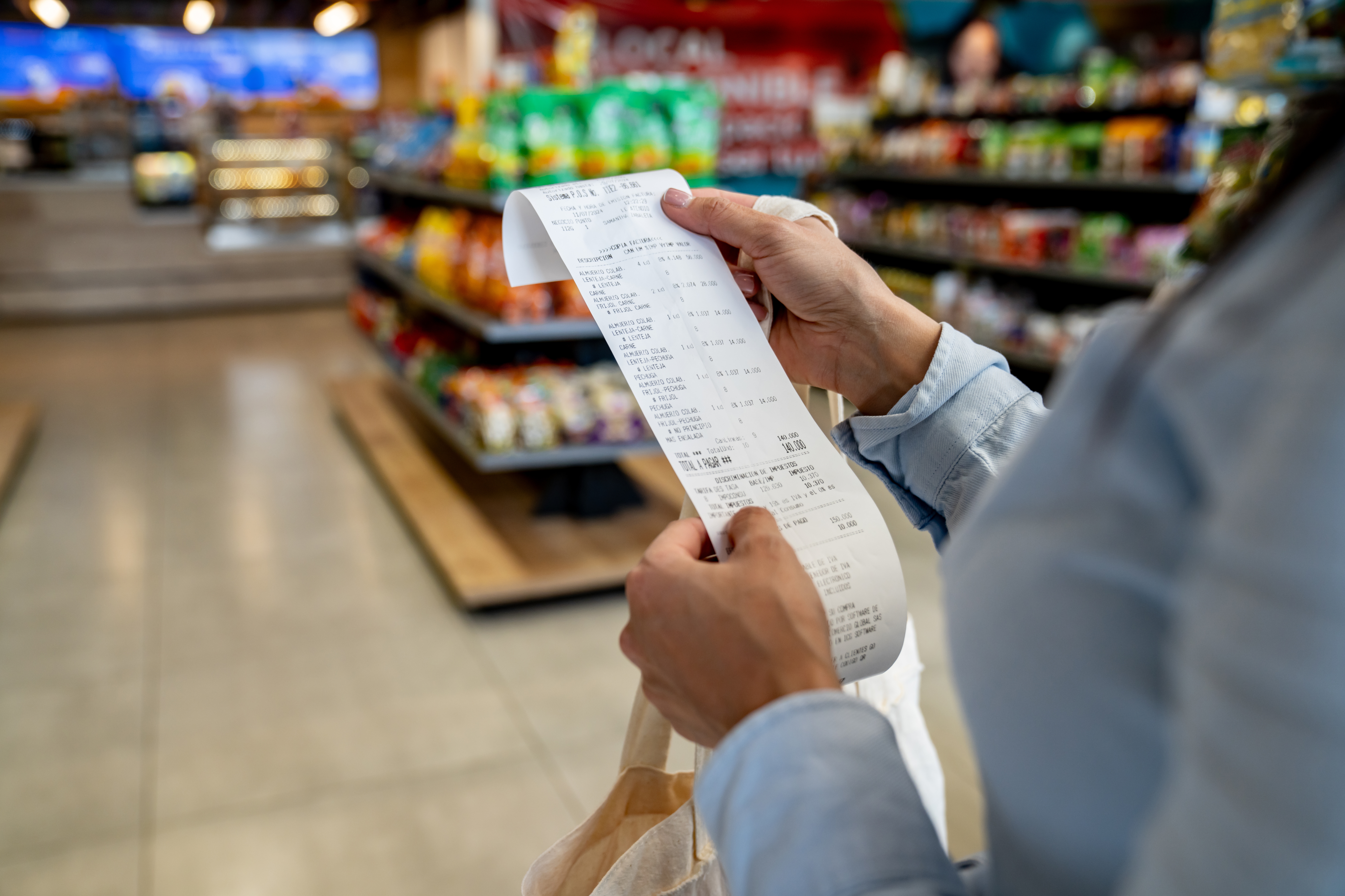 Person holding a agelong  receipt successful  a market  store   aisle, surrounded by shelves of packaged goods