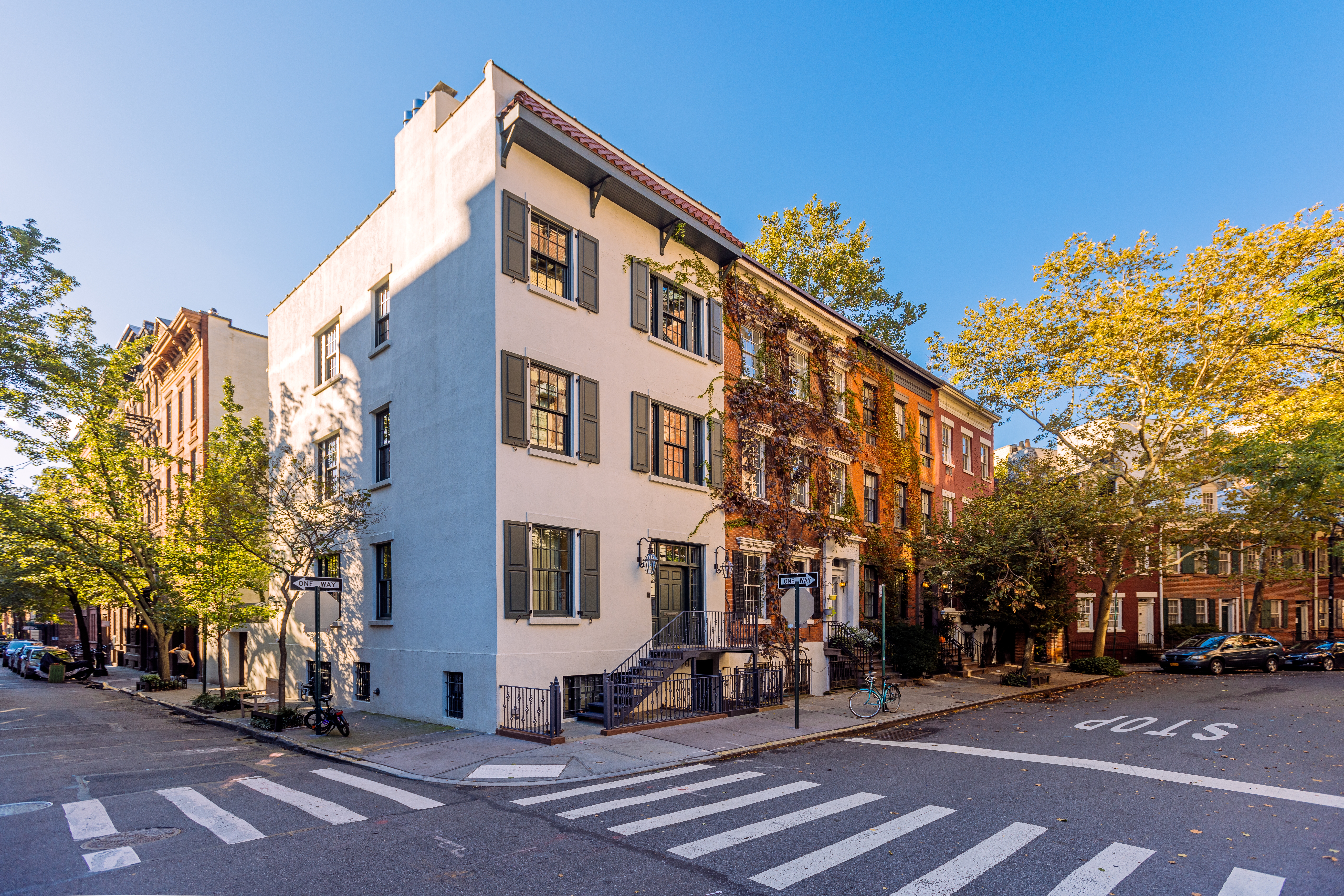 Street country   lined with historical  townhouses, tree-lined sidewalks, and a wide   bluish  sky. Quiet municipality  residential scene