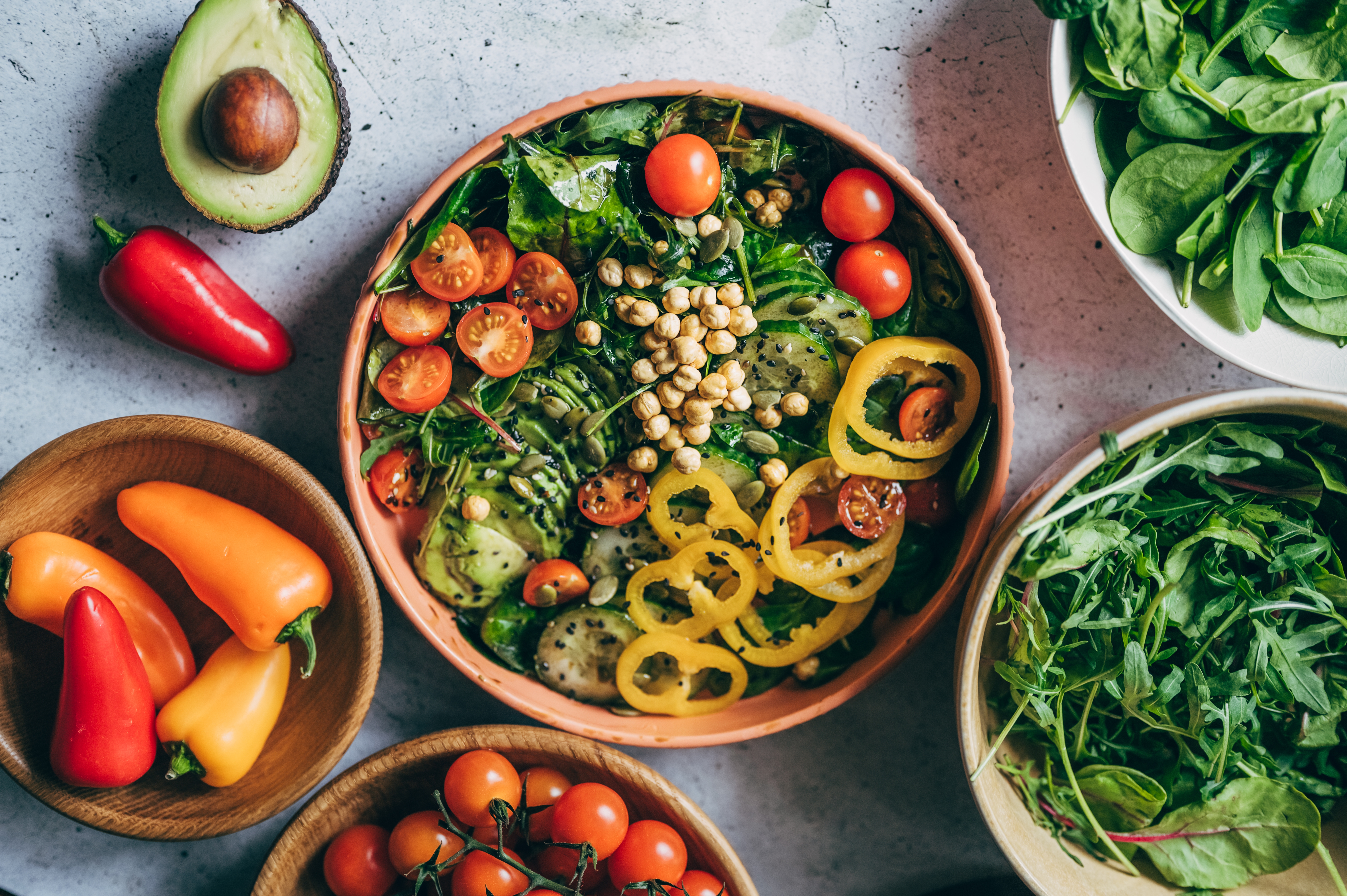 Bowl of mixed crockery   with chickpeas, cherry tomatoes, and cucumber, surrounded by caller  vegetables similar  peppers, avocado, and spinach leaves