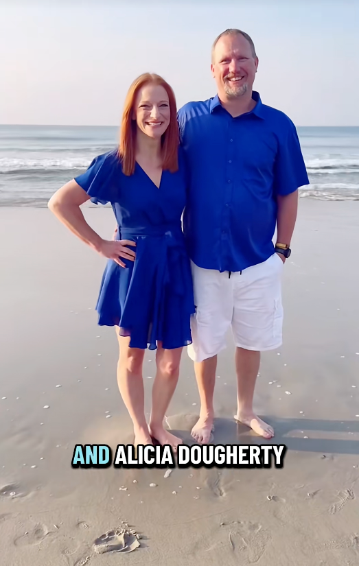 A couple stands on a beach, smiling, with gentle waves in the background; both wear casual blue outfits
