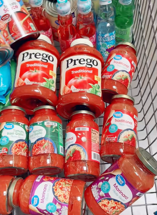 A shopping cart filled with jars of pasta sauce and cans, possibly for a cooking article or recipe inspiration
