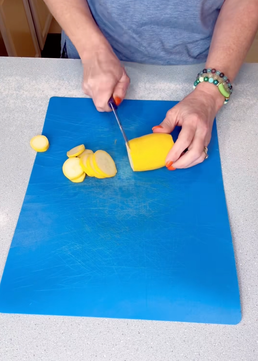 A person slices a yellow squash on a blue cutting board, showing a simple cooking preparation step