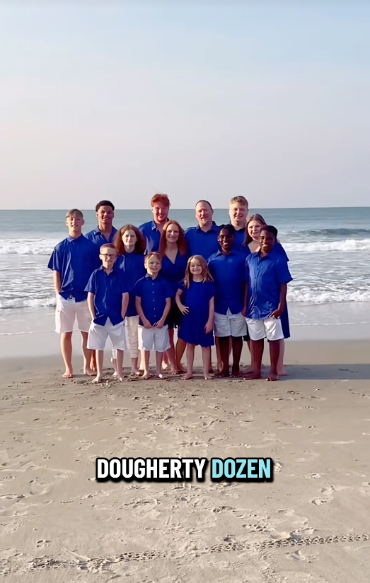 A smiling group of people stands in front of the ocean, all wearing blue outfits, with text at the bottom reading "Dougherty Dozen."