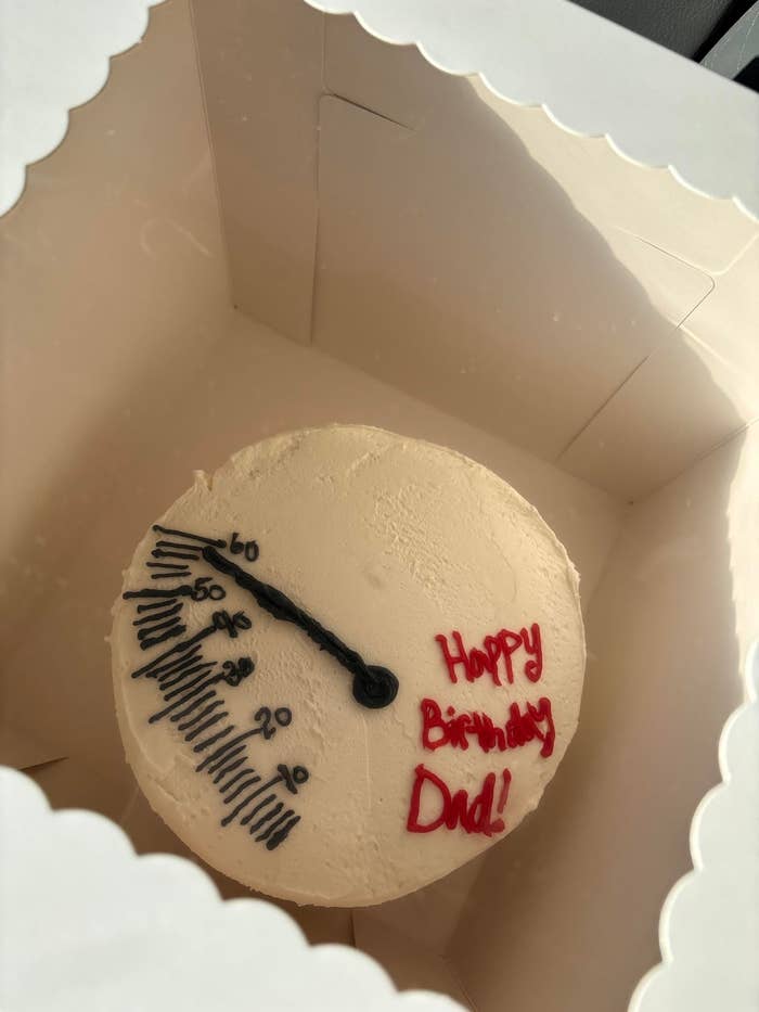 کیک گرد با طرح سرعت‌سنج نشان‌دهنده "60" و متن «تولد بابا مبارک!» در یک جعبه