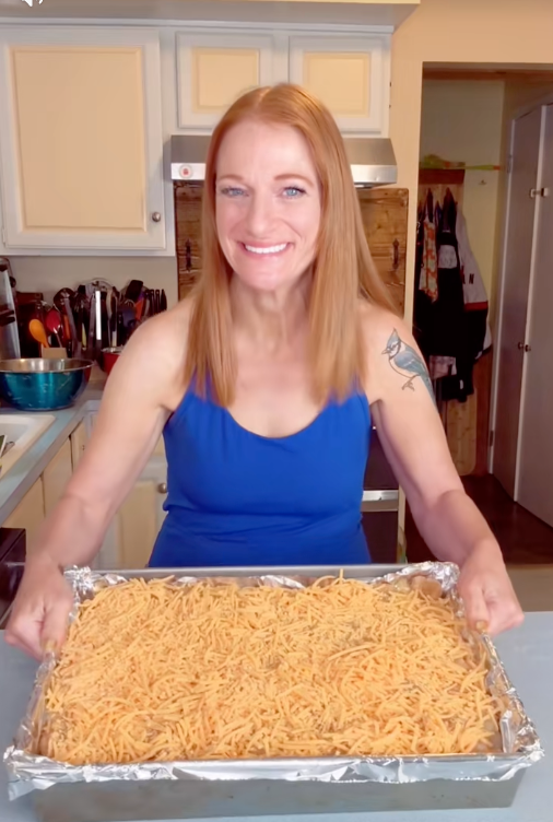 Person in kitchen holding a foil-lined baking tray with uncooked shredded ingredients