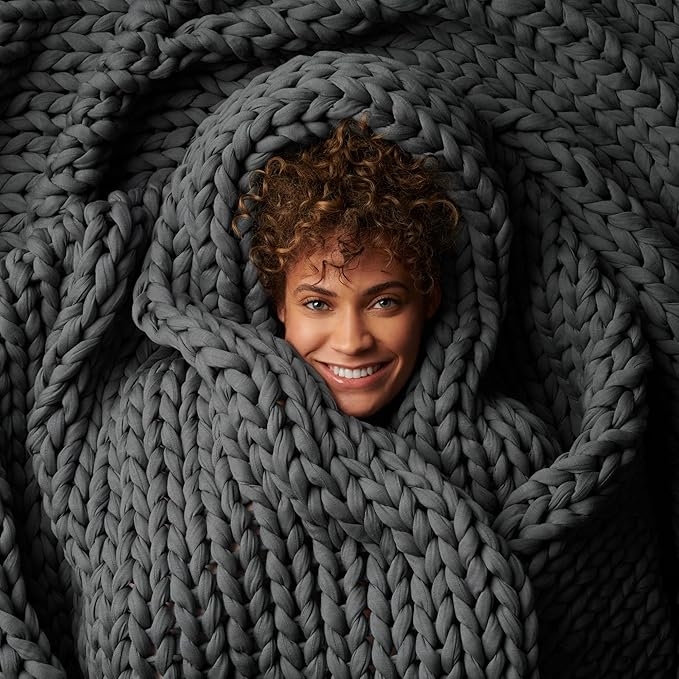 Person smiling portion    cozily wrapped successful  a large, chunky knit blanket
