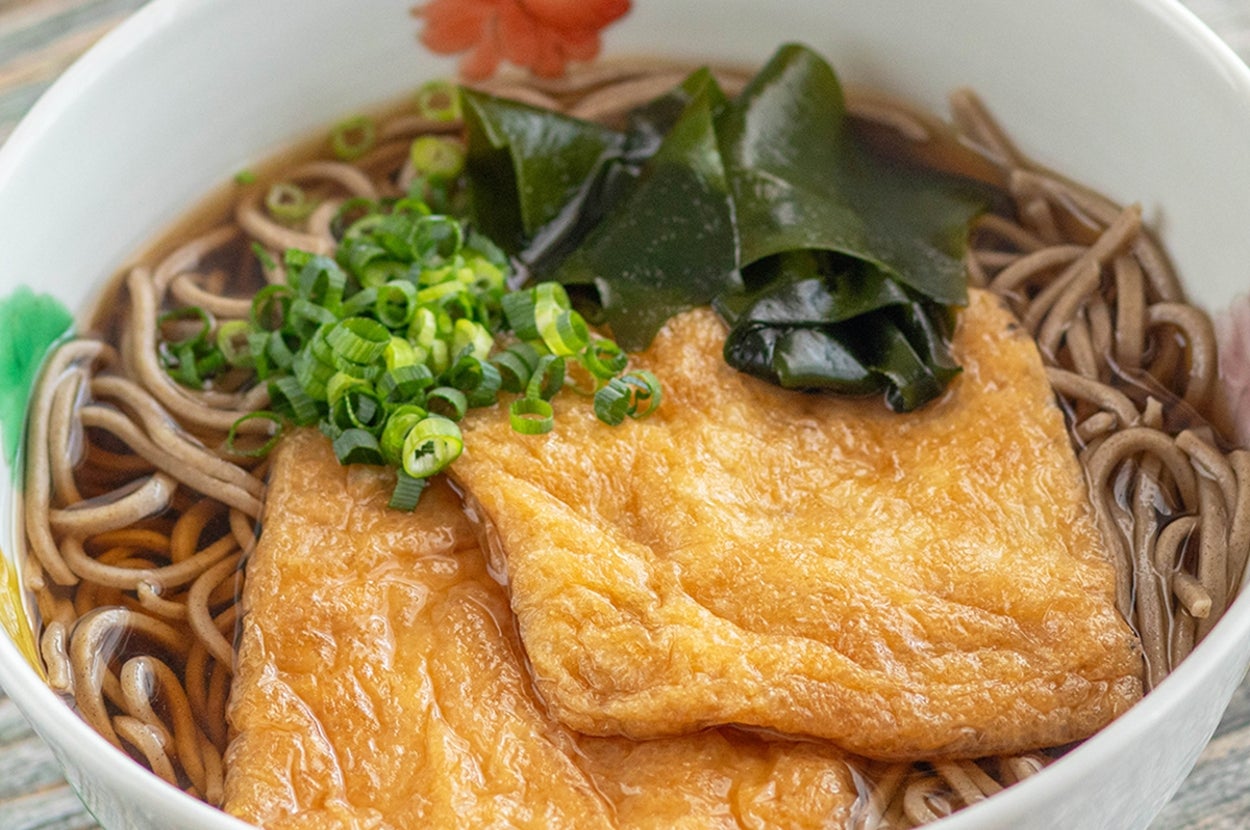 ボウルに盛られた蕎麦、油揚げ、わかめ、ねぎがのった料理。