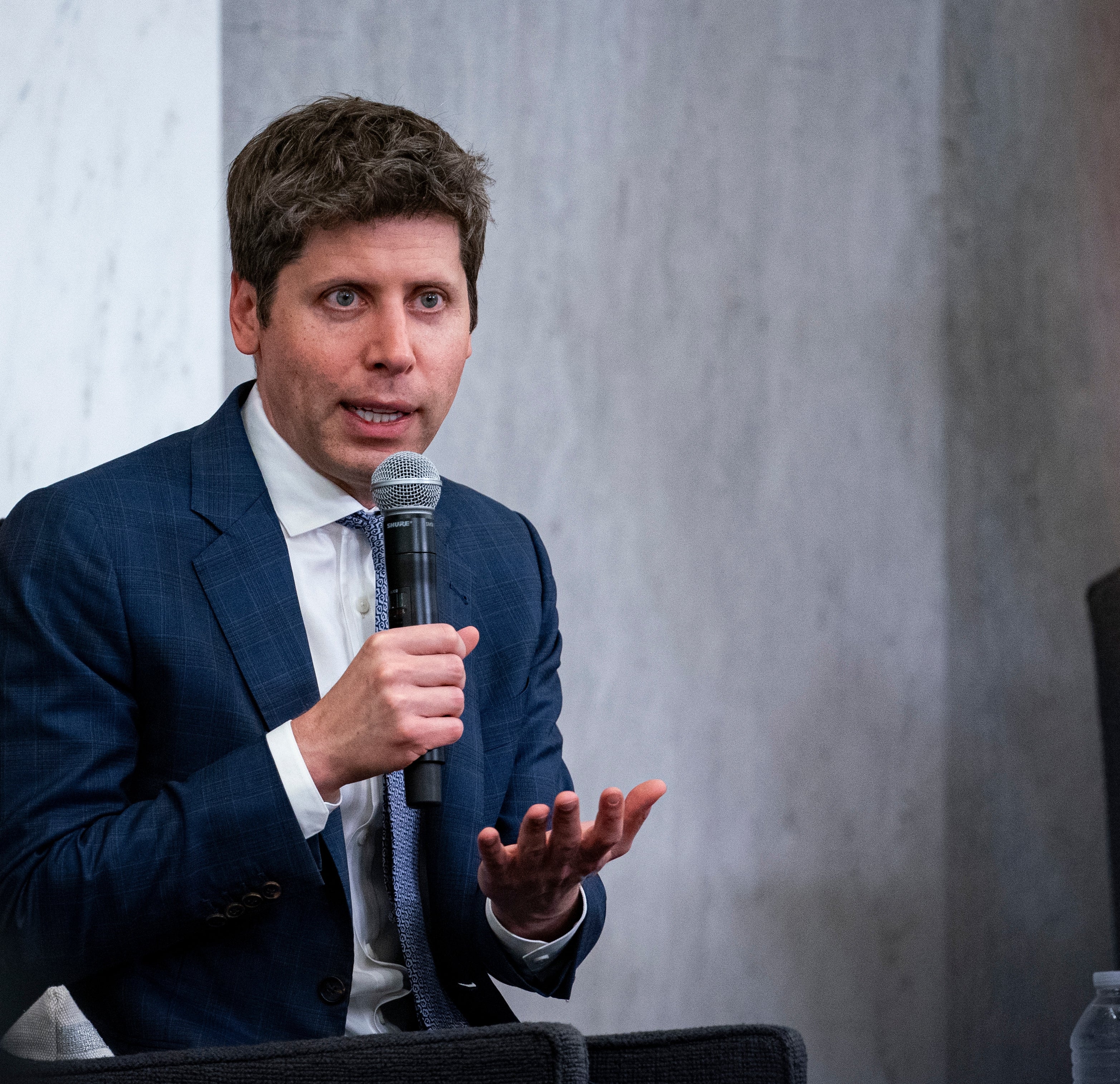 Sam Altman speaking into a microphone on stage