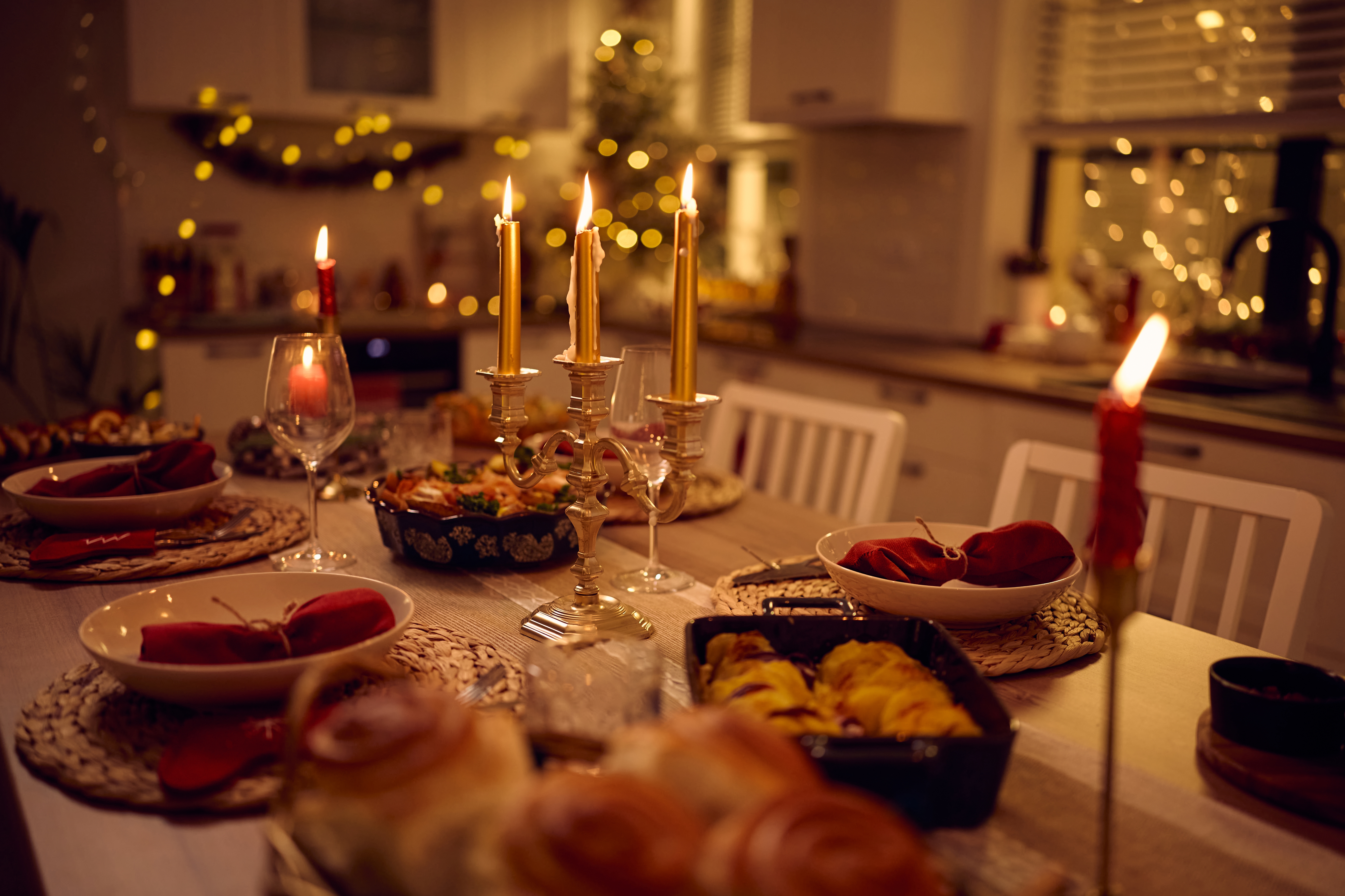 Cozy dinner table set for a festive gathering with candles, plates, and warm lighting in a kitchen decorated with holiday lights