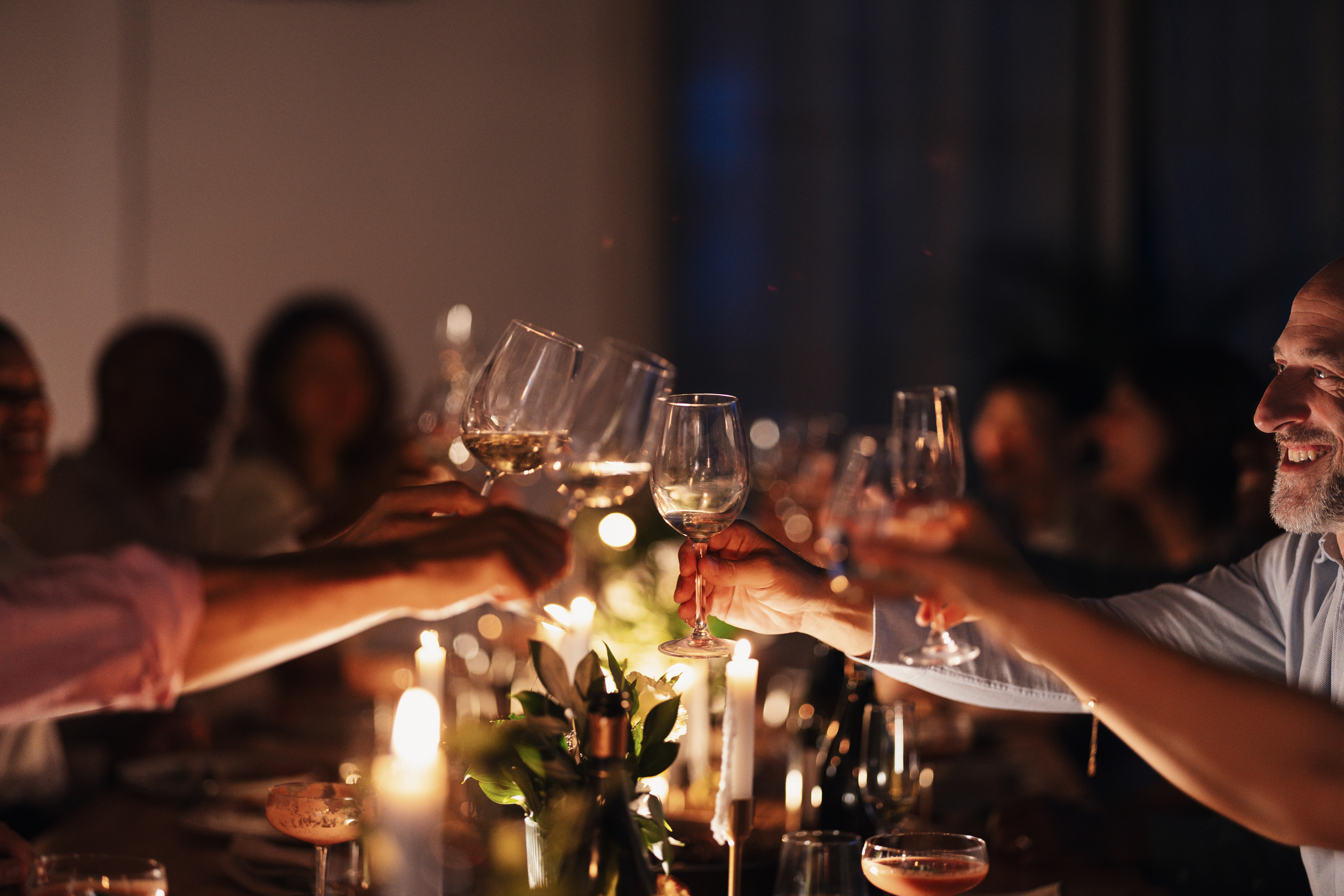 People at a dinner party clinking glasses in a toast, surrounded by candles and table decor
