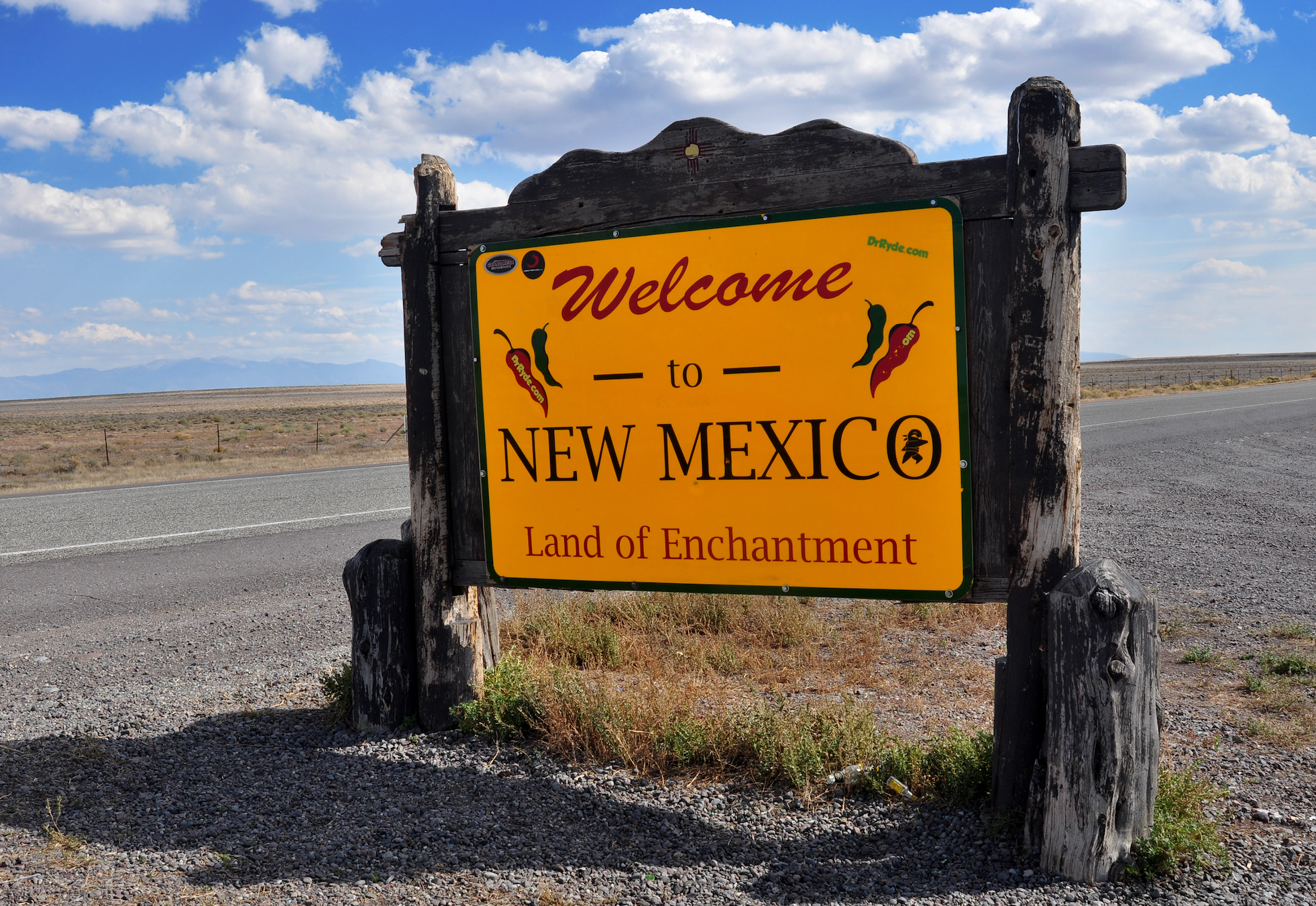 Welcome to New Mexico motion   connected  a agrarian  roadside with distant   mountains and a partially  cloudy sky