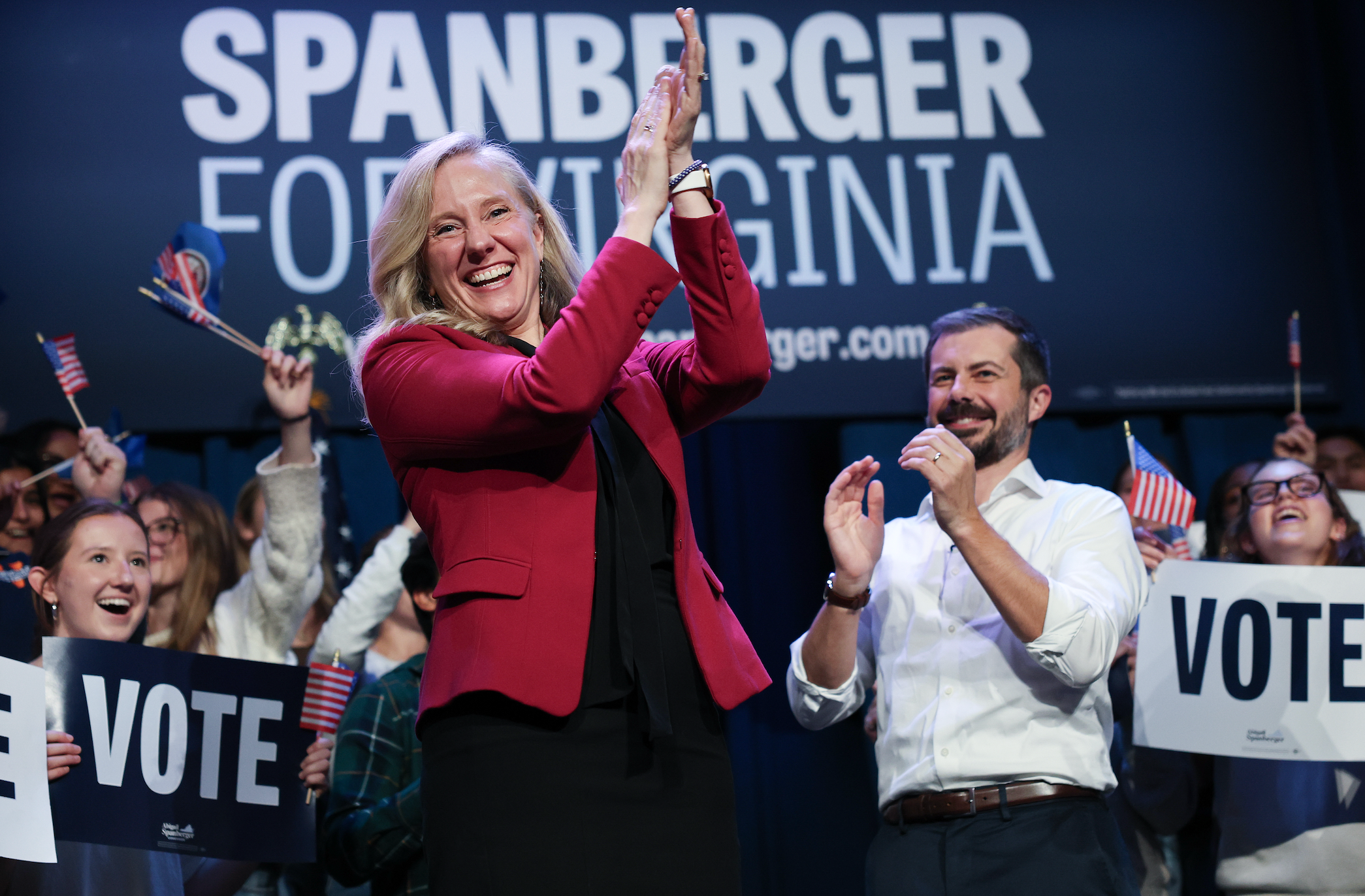 En kvinne i blazer klapper på scenen med supportere som holder «Vote" tegn