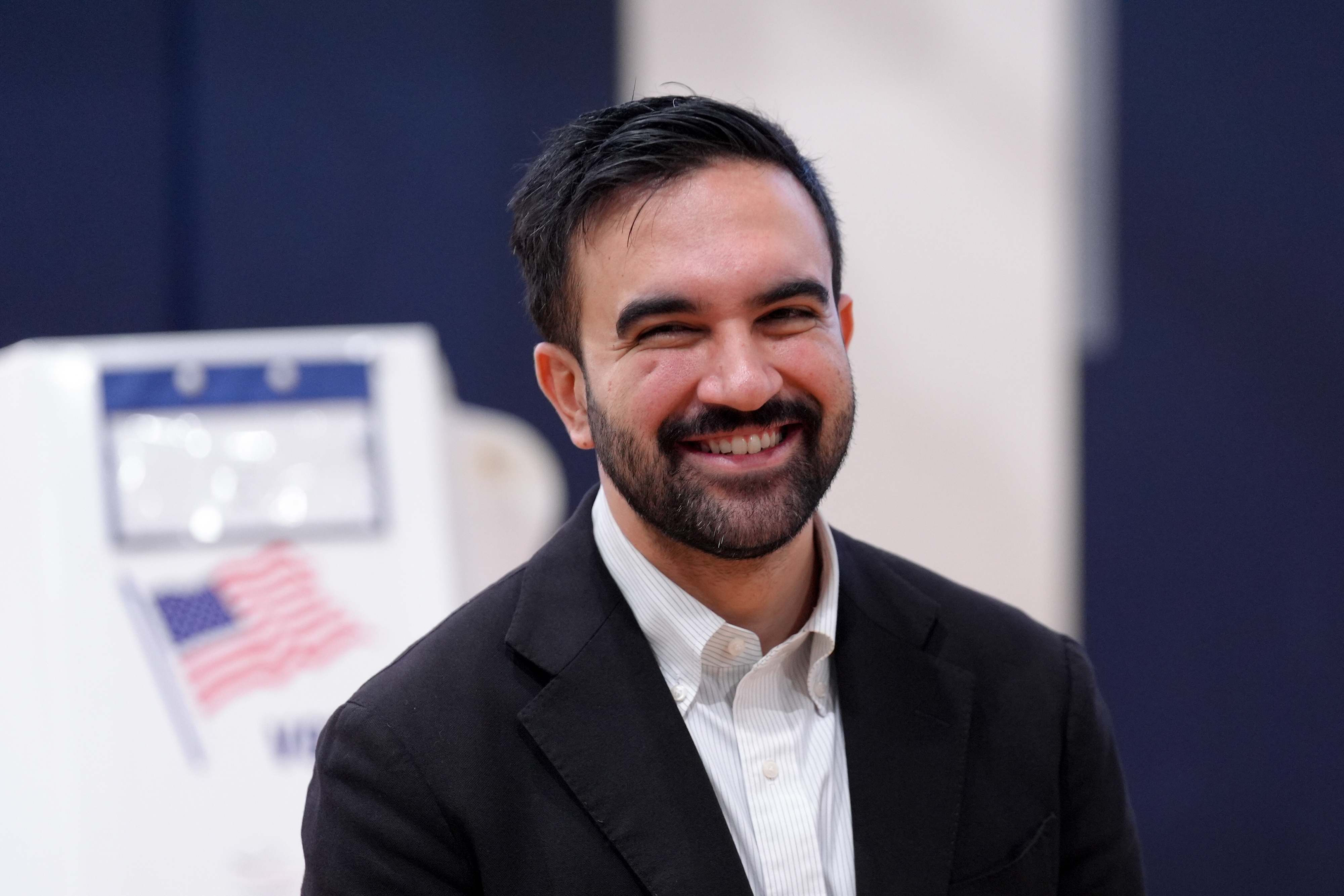 A idiosyncratic   successful  a suit   smiling, lasting  indoors adjacent   a U.S. voting booth with an American flag