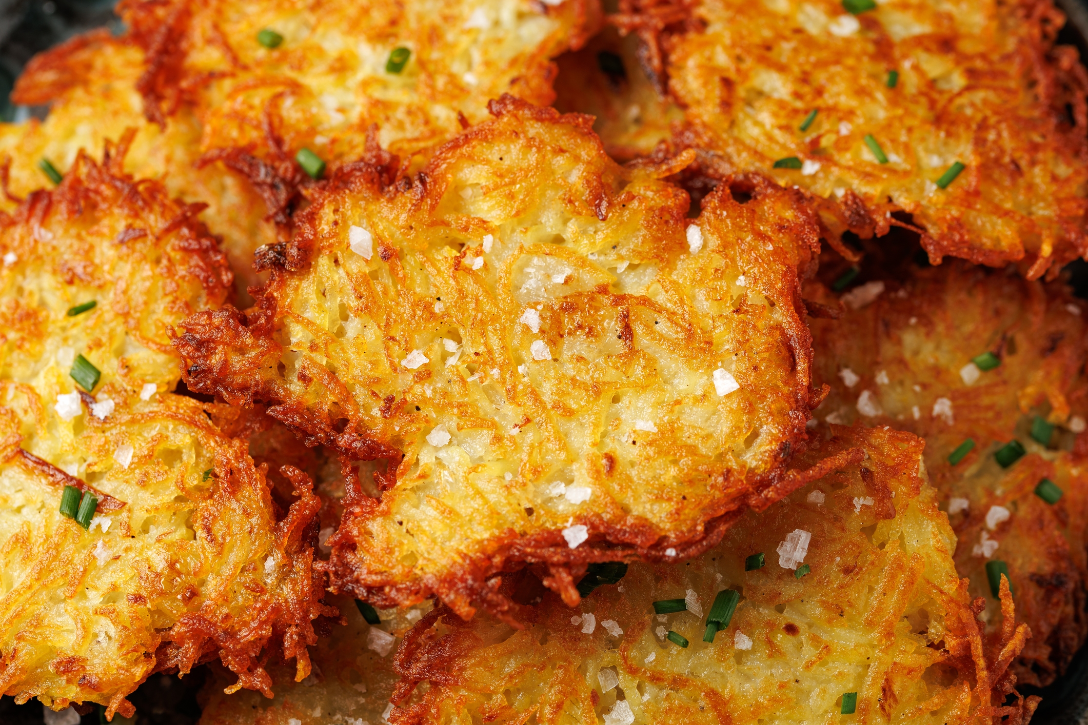 Crispy, golden-brown potato latkes garnished with chopped chives and sprinkled with coarse salt