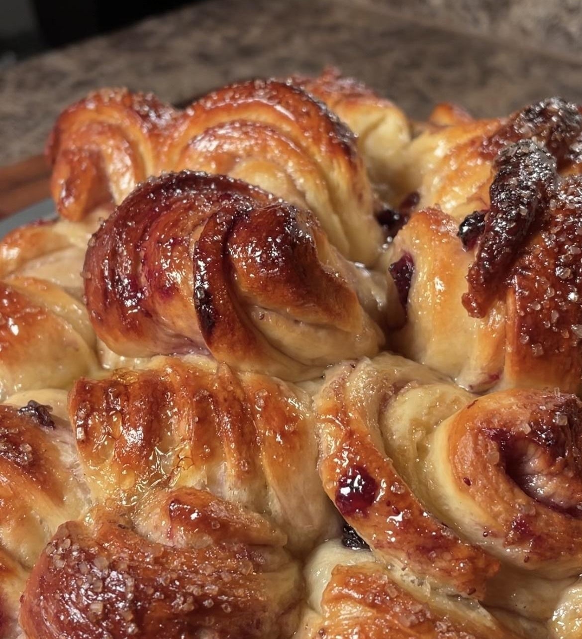 A freshly-baked, golden croissant bread with a crispy crust, topped with sugar crystals, sitting on a kitchen counter