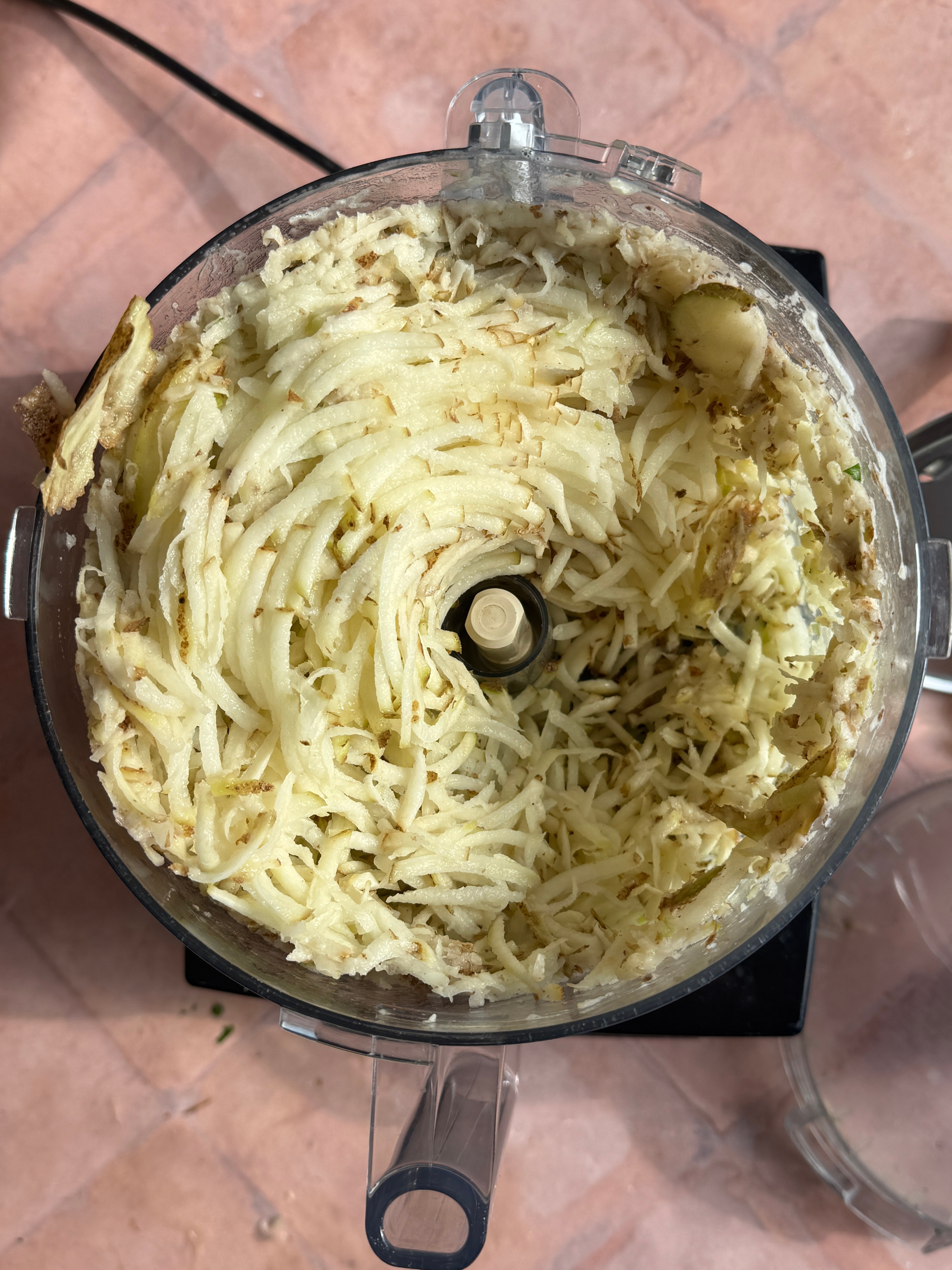 Shredded potatoes in a food processor bowl on a kitchen counter