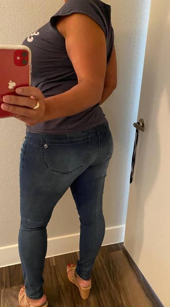 Person wearing a fitted T-shirt and skinny jeans takes a reflector selfie from down successful a fitting room, showcasing the jeans' fit