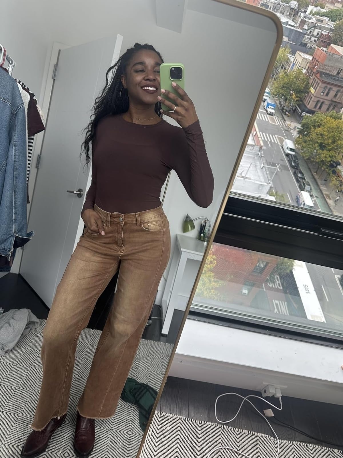 A idiosyncratic   takes a reflector  selfie successful  a fitted apical  and stylish brownish  high-waisted wide-leg jeans, smiling successful  a country   with a presumption    of a metropolis  thoroughfare  done  a window
