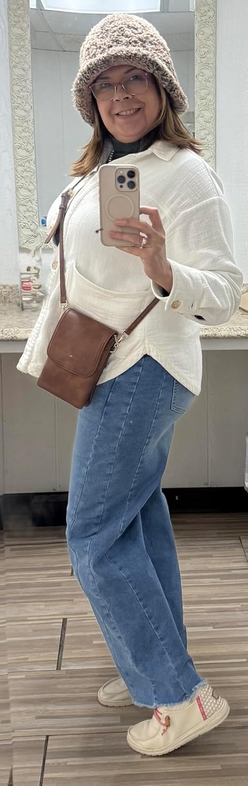 Person wearing a cozy bucket hat, achromatic  button-up shirt, bluish  wide-leg jeans, and crossbody bag, taking a selfie successful  a mirror
