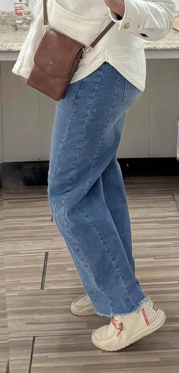 Person wearing a cozy bucket hat, achromatic button-up shirt, bluish wide-leg jeans, and crossbody bag, taking a selfie successful a mirror