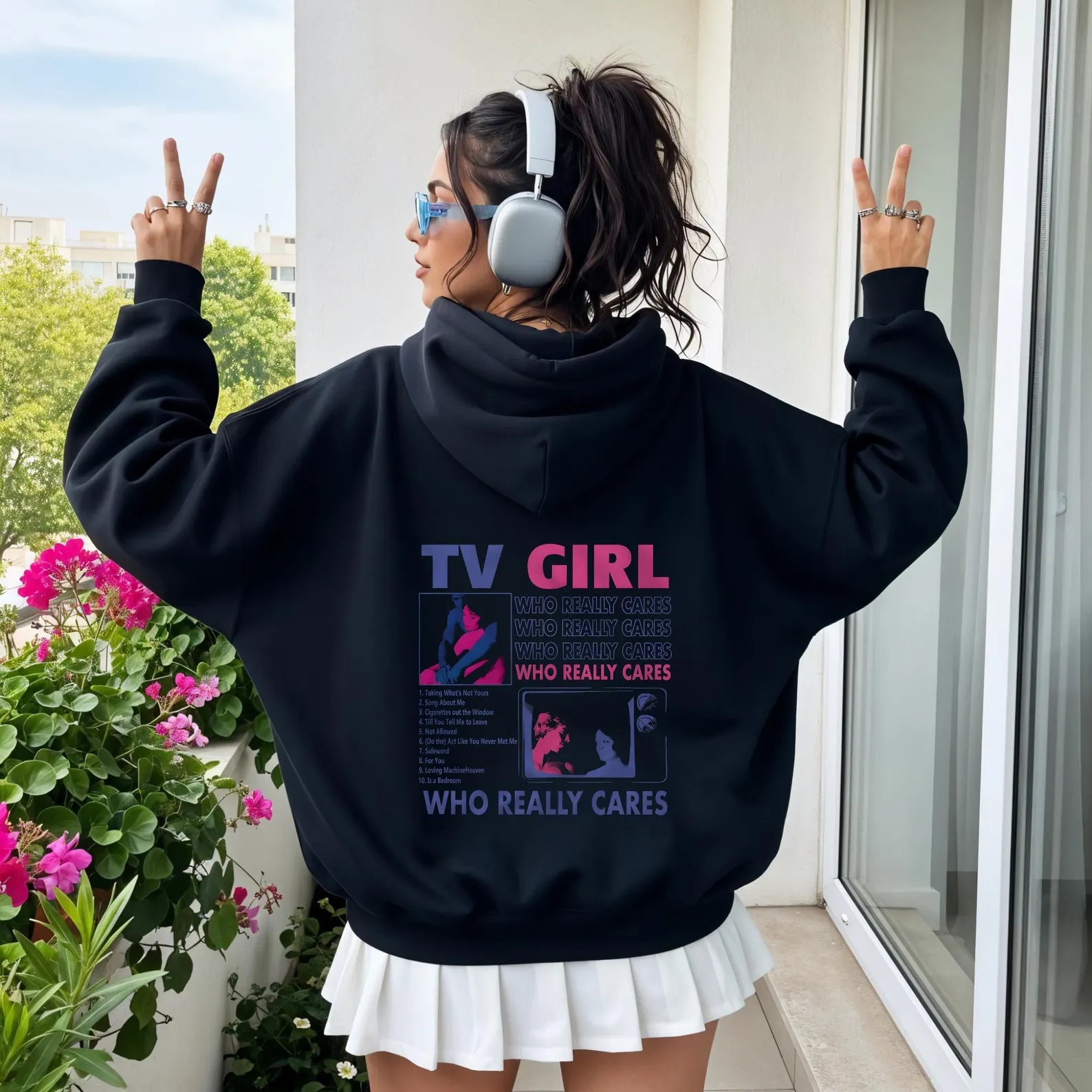Person wearing headphones and a achromatic  hoodie with graphic text. They basal   connected  a balcony, giving bid    signs beside potted plants