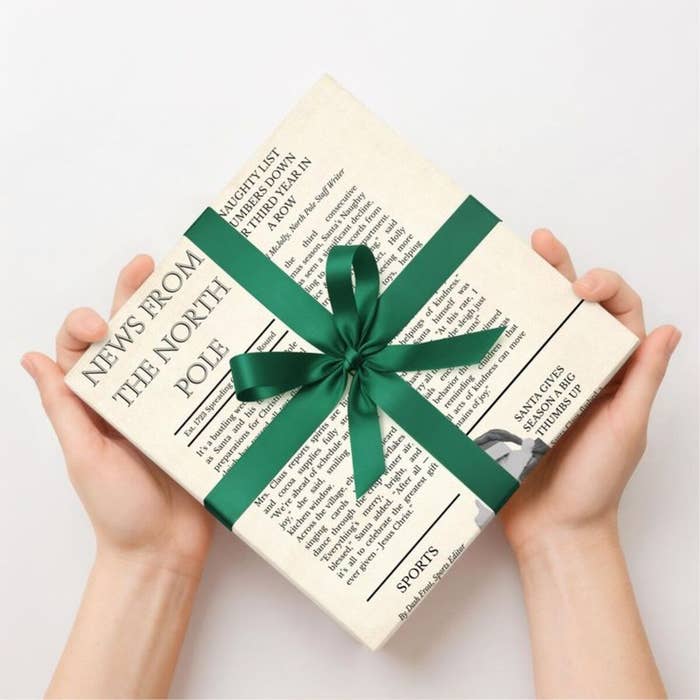 Caja envuelta como periódico titulado &quot;News from the North Pole&quot; con un lazo verde. Decoración navideña o regalo temático