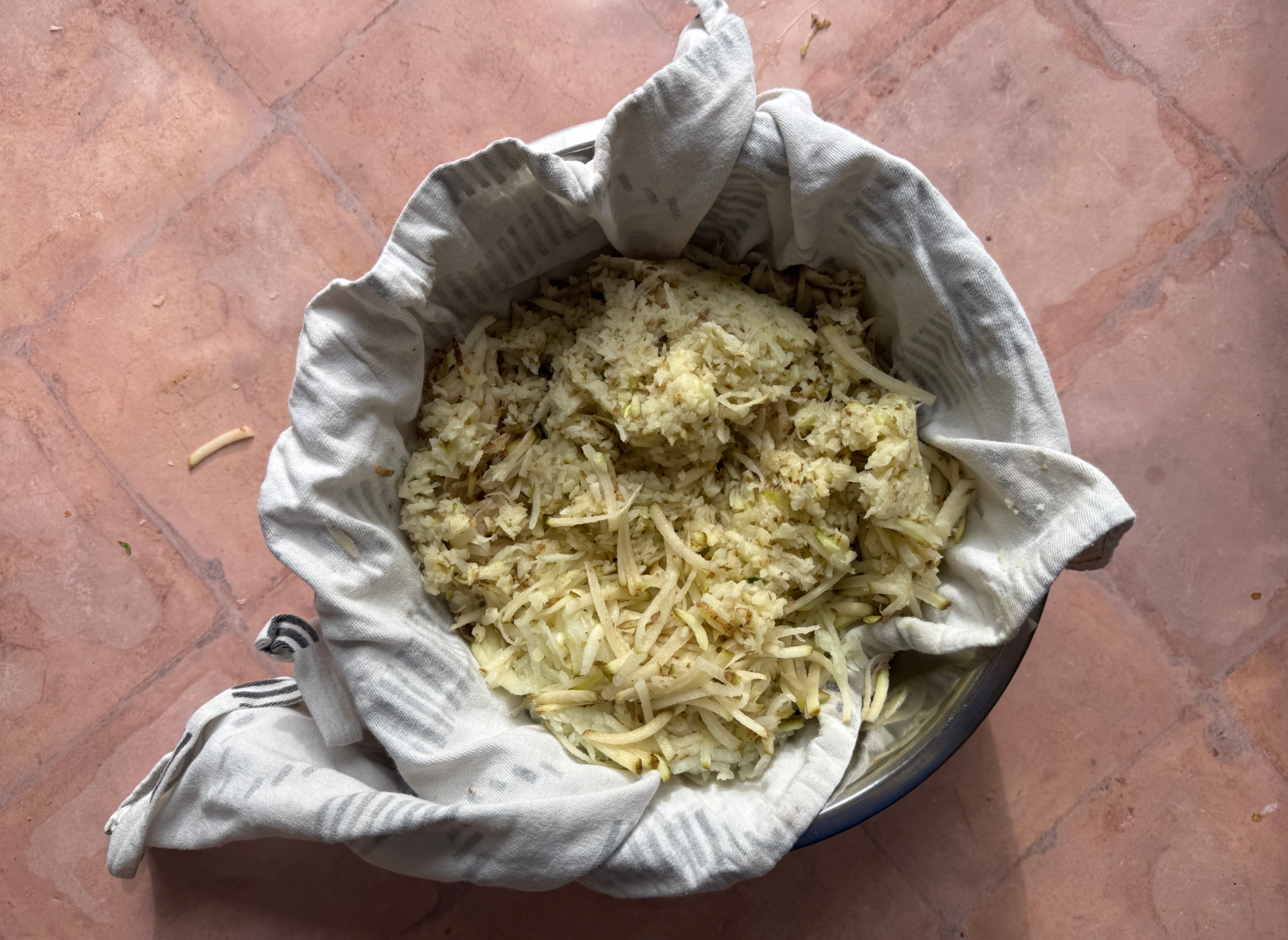 Shredded potatoes and onions in a cloth-lined bowl, possibly being prepared for cooking or draining