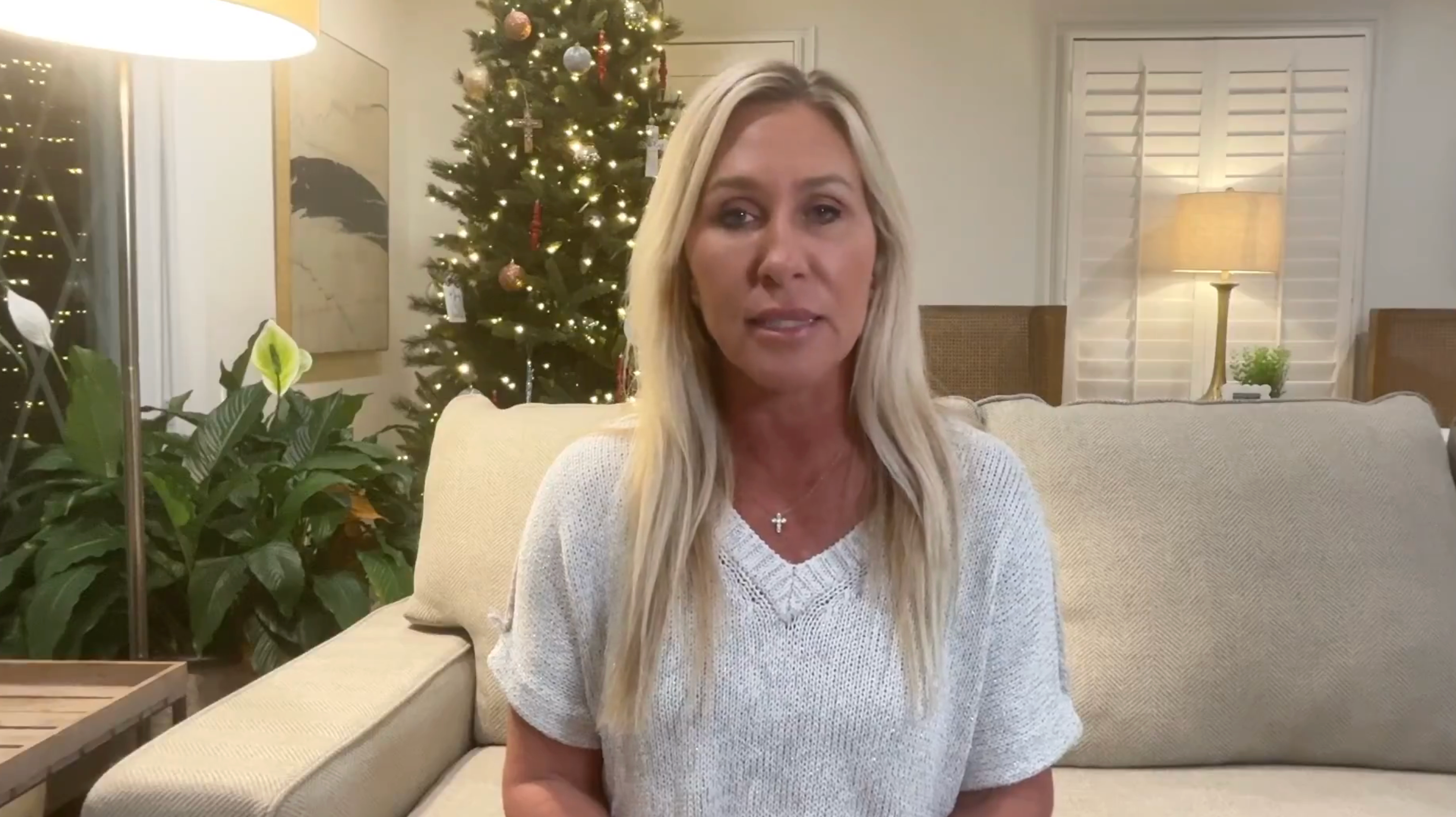 En person sitter på en sofa i en stue dekorert med et juletre og planter