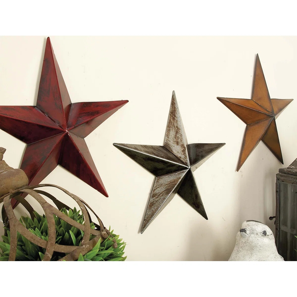 Three decorative metallic  stars successful  varying sizes are mounted connected  a partition  supra  a sculpture and a tiny  plant
