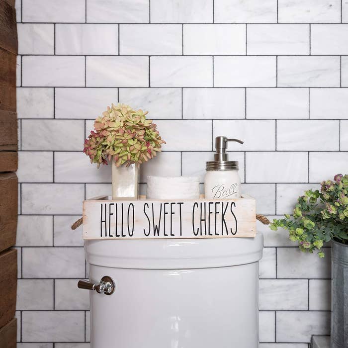 Bathroom decor connected  a toilet tank, featuring a motion   saying "Hello Sweet Cheeks," with a angiosperm  vase and soap dispenser