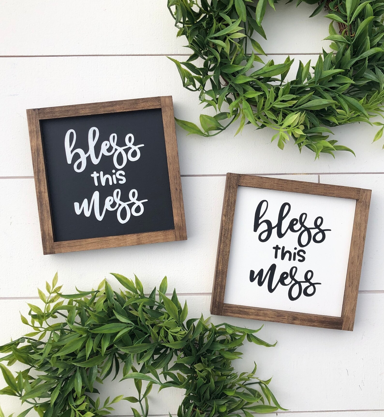 Two framed signs with "Bless this mess" text, surrounded by greenery connected  a woody  background
