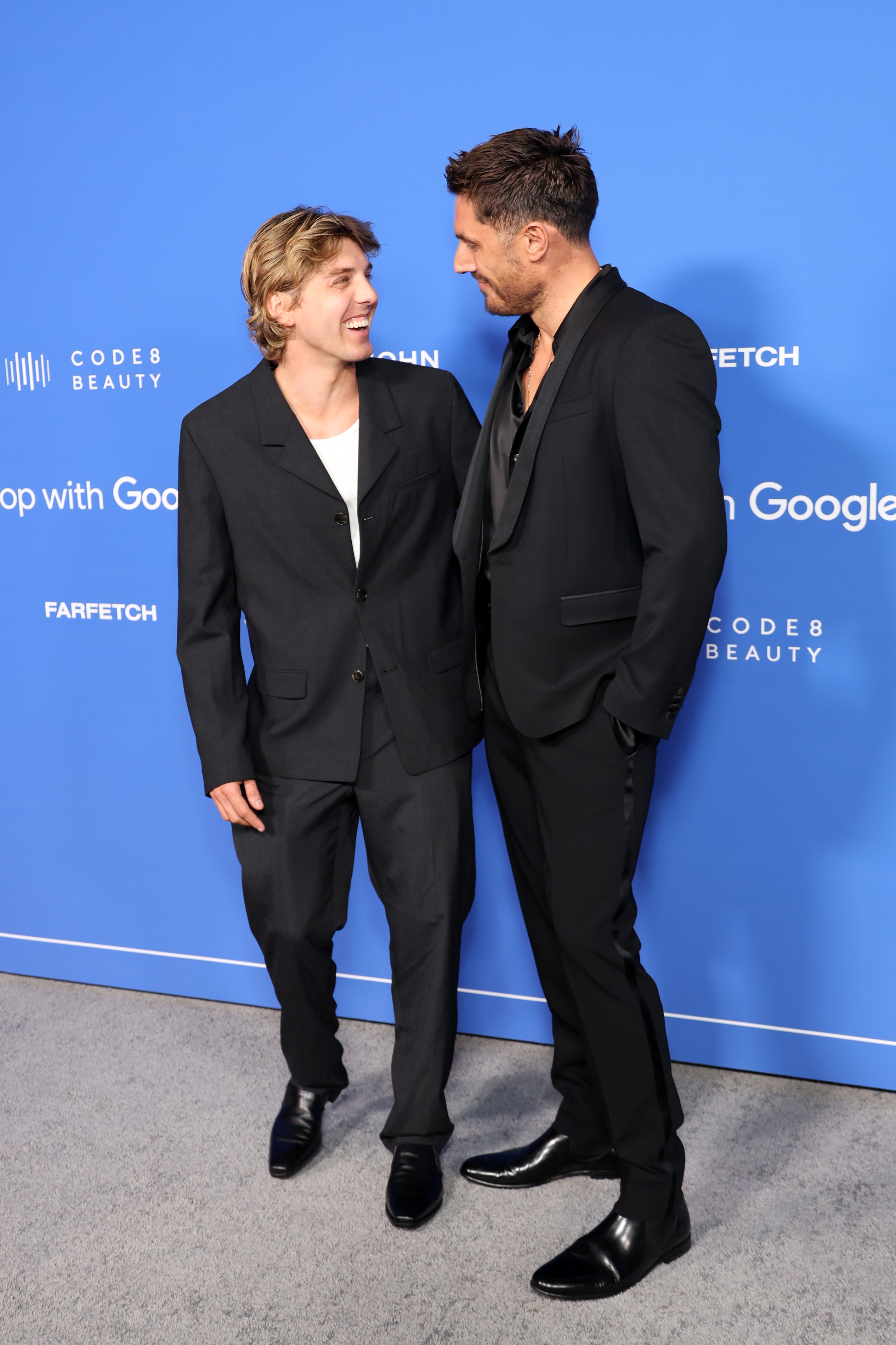 Two radical   successful  stylish achromatic  suits, smiling astatine  each   different   connected  a bluish  carpet event