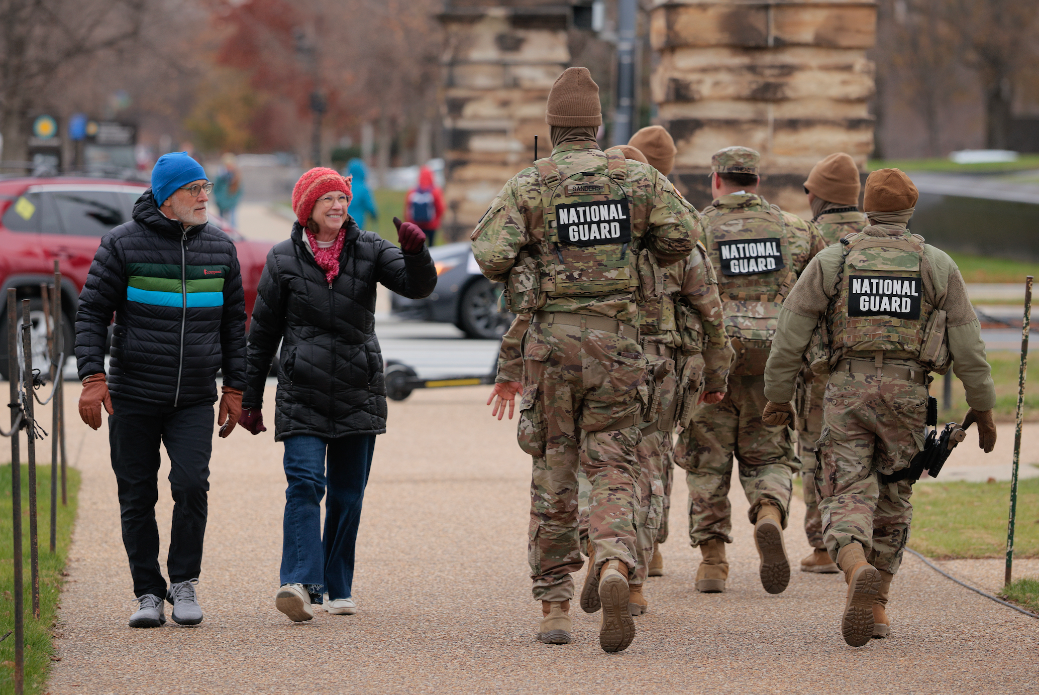 People walking adjacent National Guard members successful uniform, who are wearing protective gear. A casual and unafraid thoroughfare scene