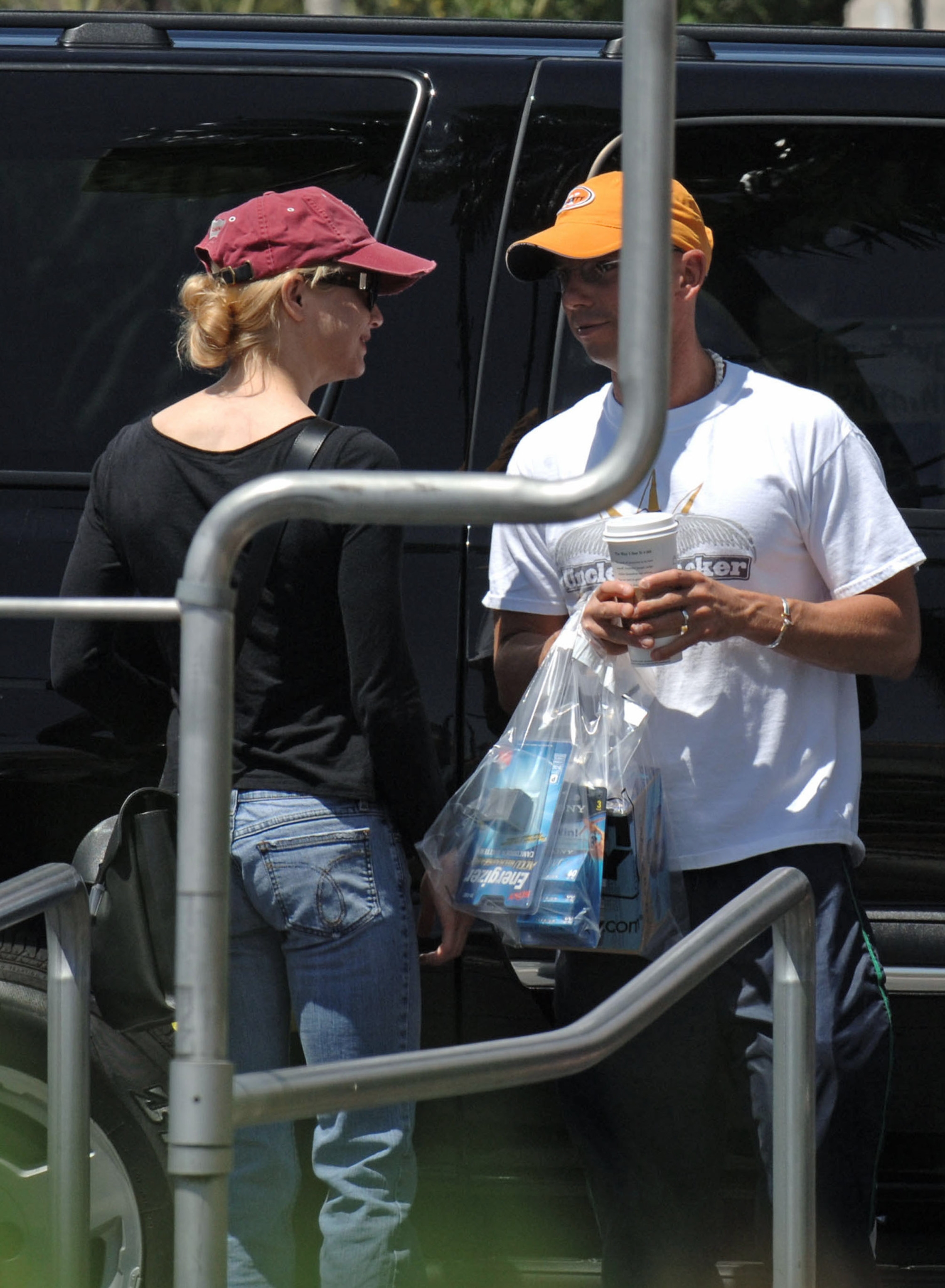 Two radical   basal   by a vehicle, facing each   different   and smiling. They are casually dressed, with shot   caps and jeans, holding a portion  and a integrative  bag