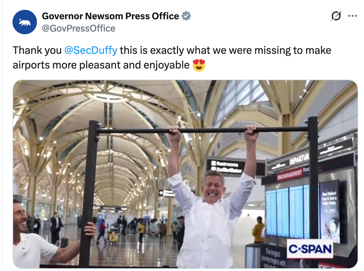 Mann i hvit skjorte hengende fra uttrekkbarer på flyplassen, smilende, med reisende og flyplassskilt i bakgrunnen