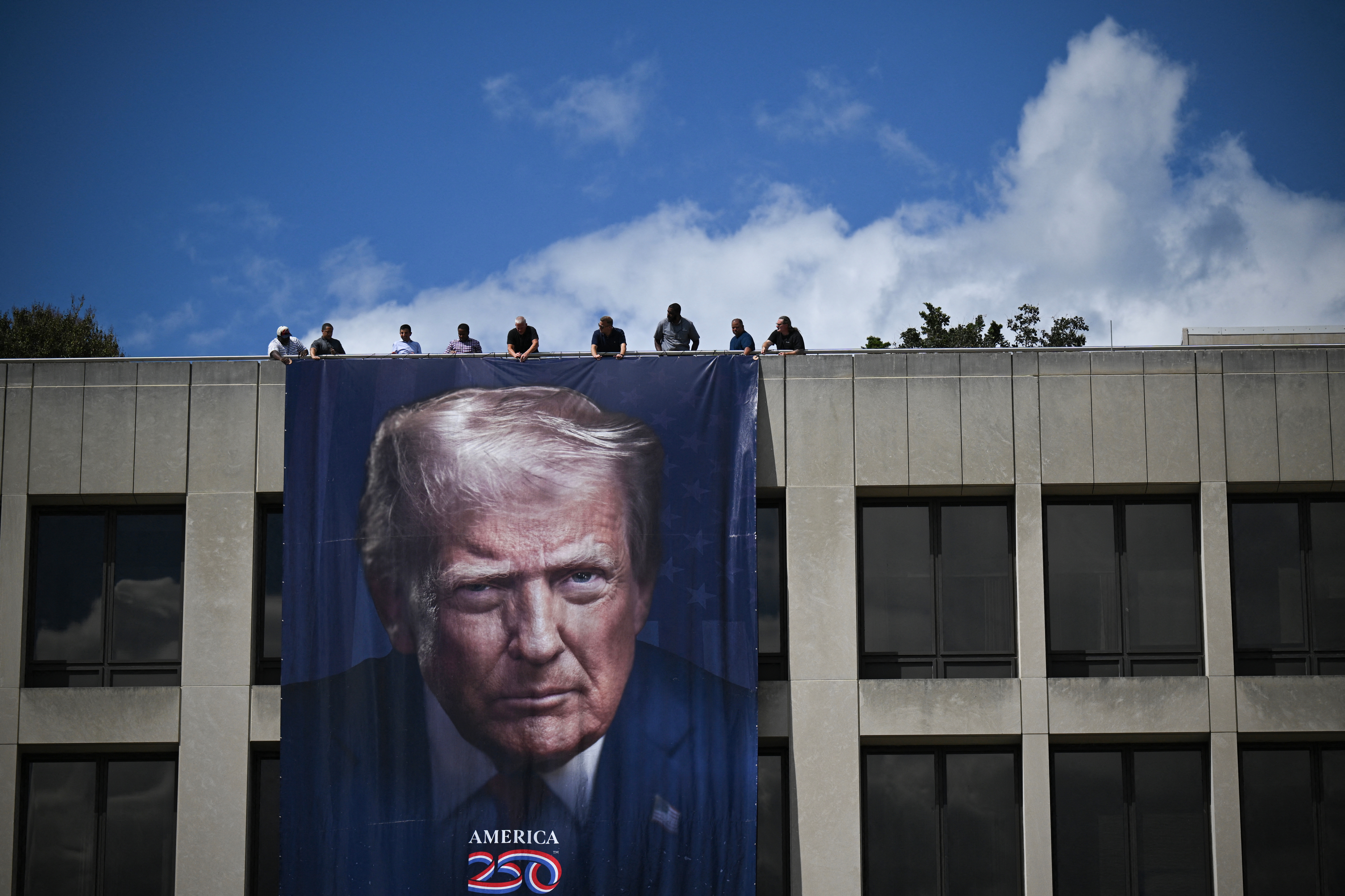Large banner of a antheral with a superior look hangs connected a building. People are lasting connected the extortion supra it