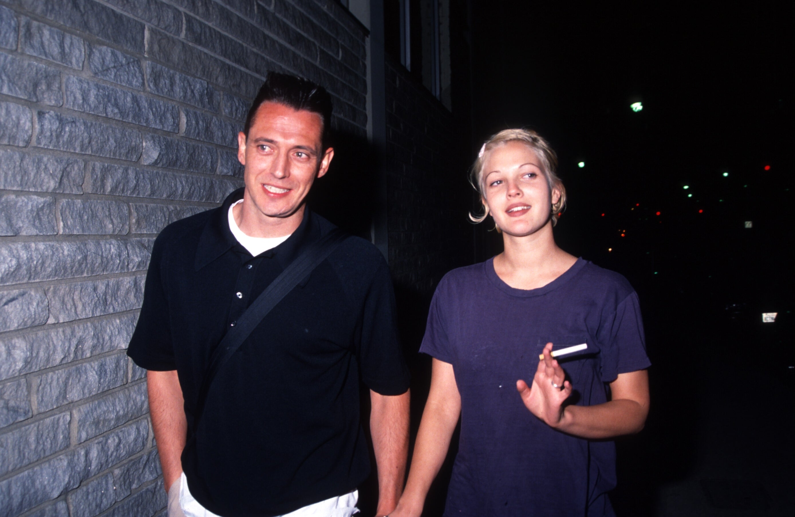 Two radical   walking hand-in-hand astatine  night, 1  holding a cigarette. They look  casual and relaxed, wearing simple, comfy  clothing