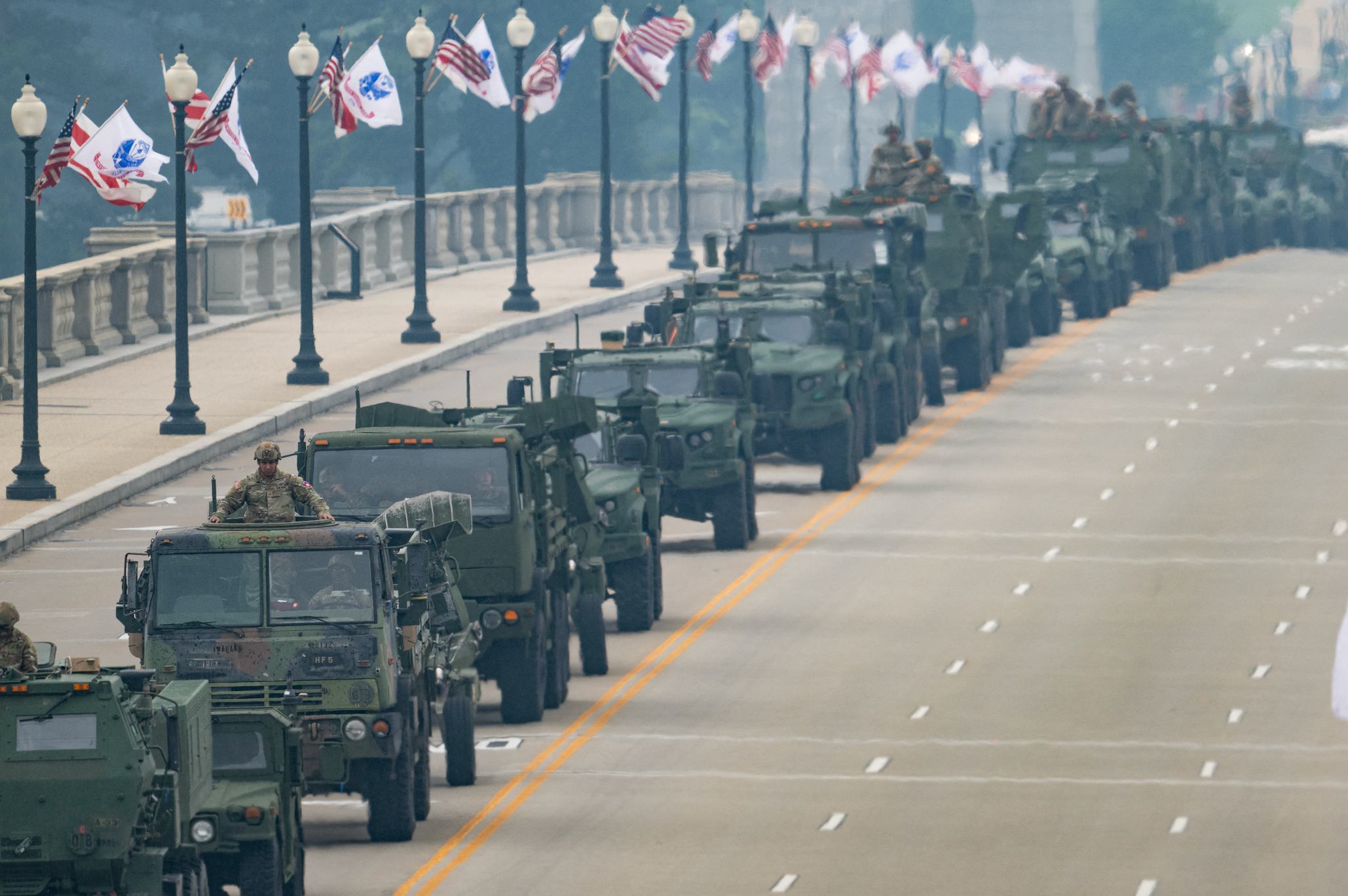 Military vehicles and unit successful a convoy connected a metropolis thoroughfare lined with flags connected lamp posts