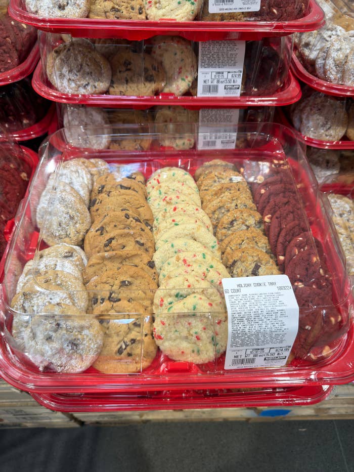 Assorted cookies in a clear plastic tray with chocolate chip, sprinkle, powdered sugar, and red velvet varieties displayed at a store