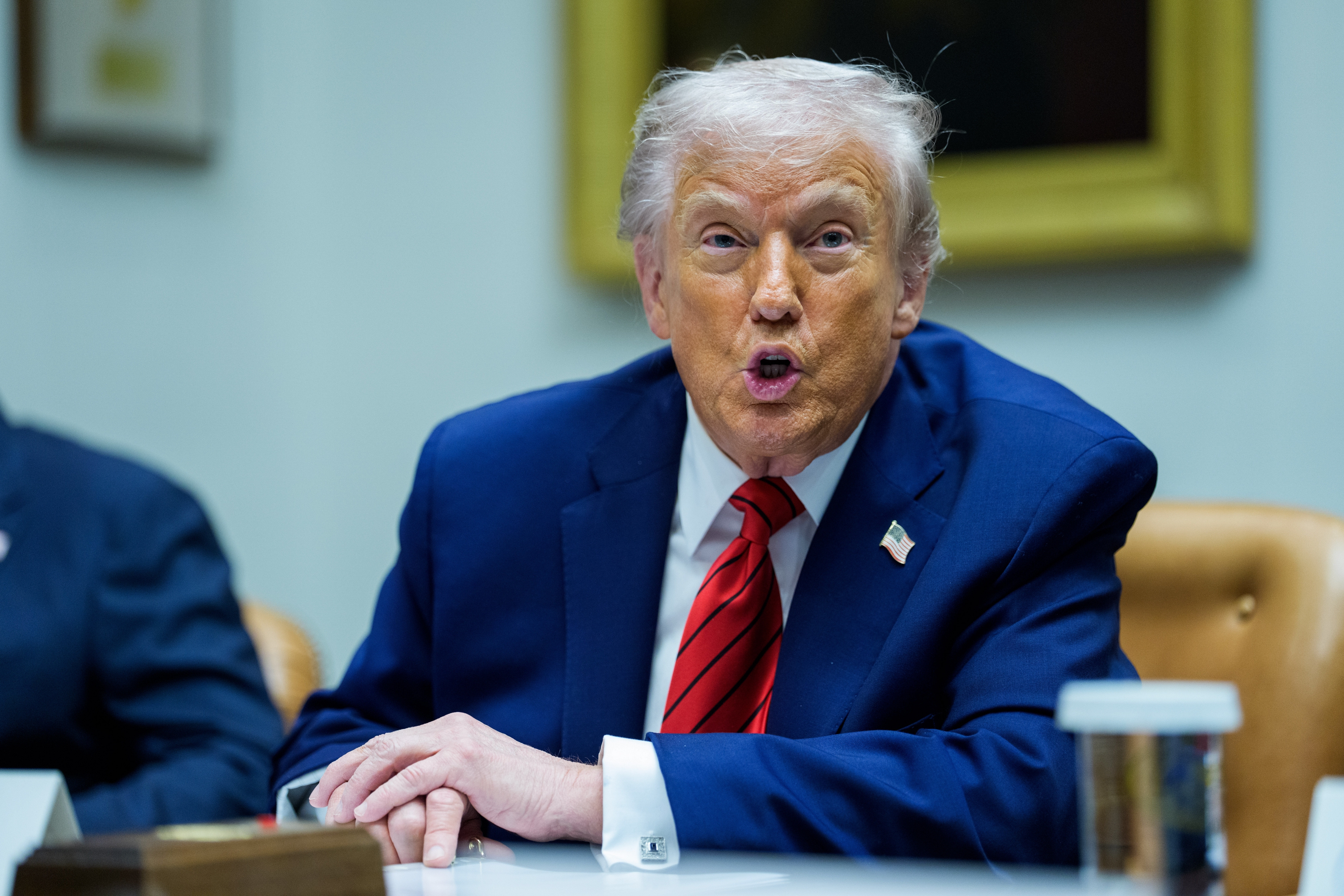 En person i dress taler på et møte, sittende ved et bord. De fremstår som animerte og engasjerte i diskusjon