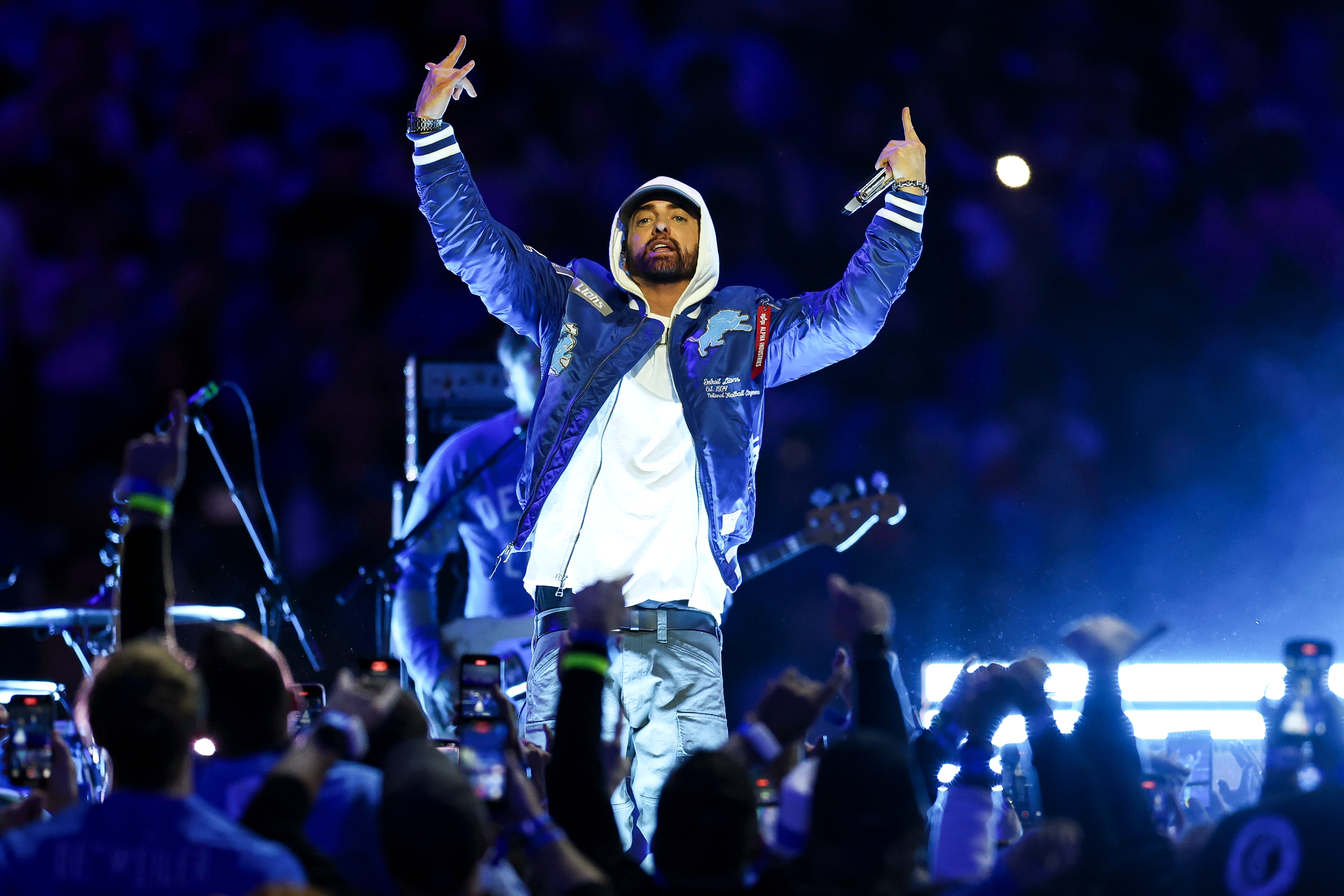 Performer connected  signifier    with raised arms, wearing a casual overgarment   and pants, surrounded by cheering crowd