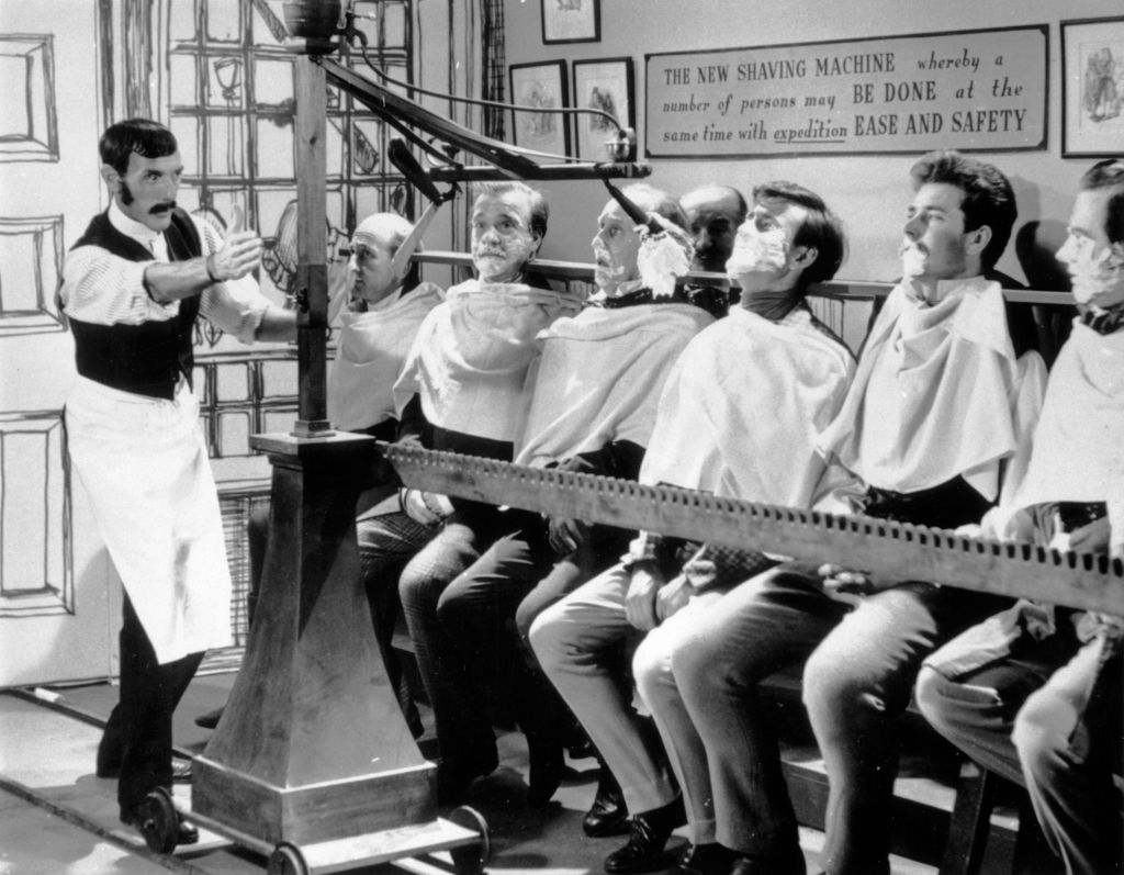 Barber operates a vintage multi-person shaving instrumentality   connected  seated men, showcasing humanities  shaving exertion   with a absorption   connected  efficiency