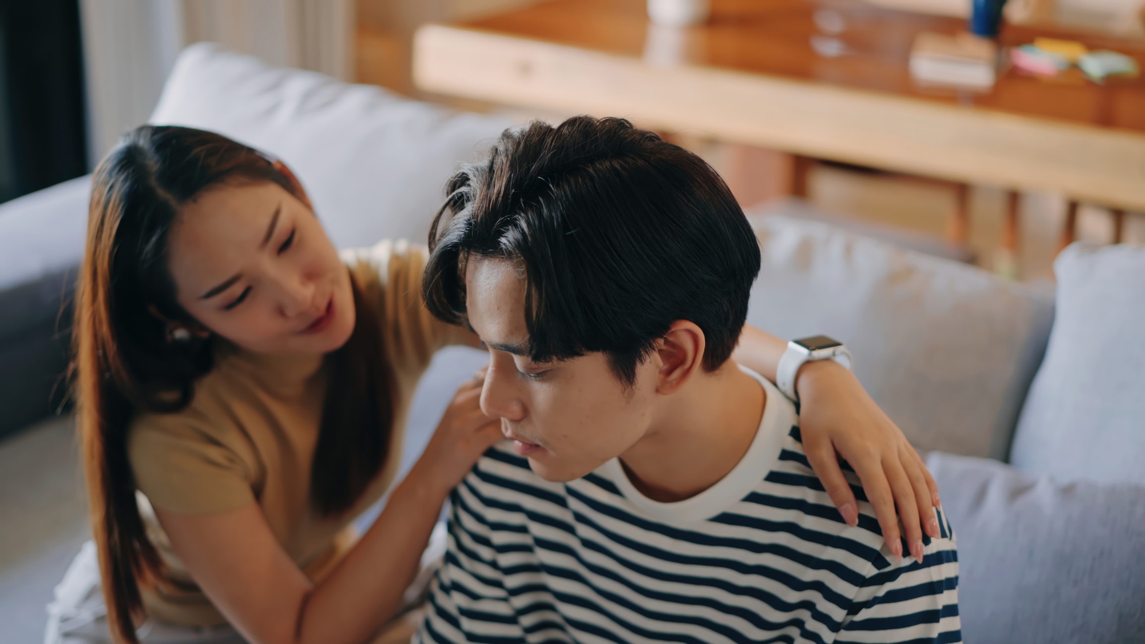 Two radical   sitting connected  a couch, 1  comforting the different   by putting a manus  connected  their shoulder, with a caring expression